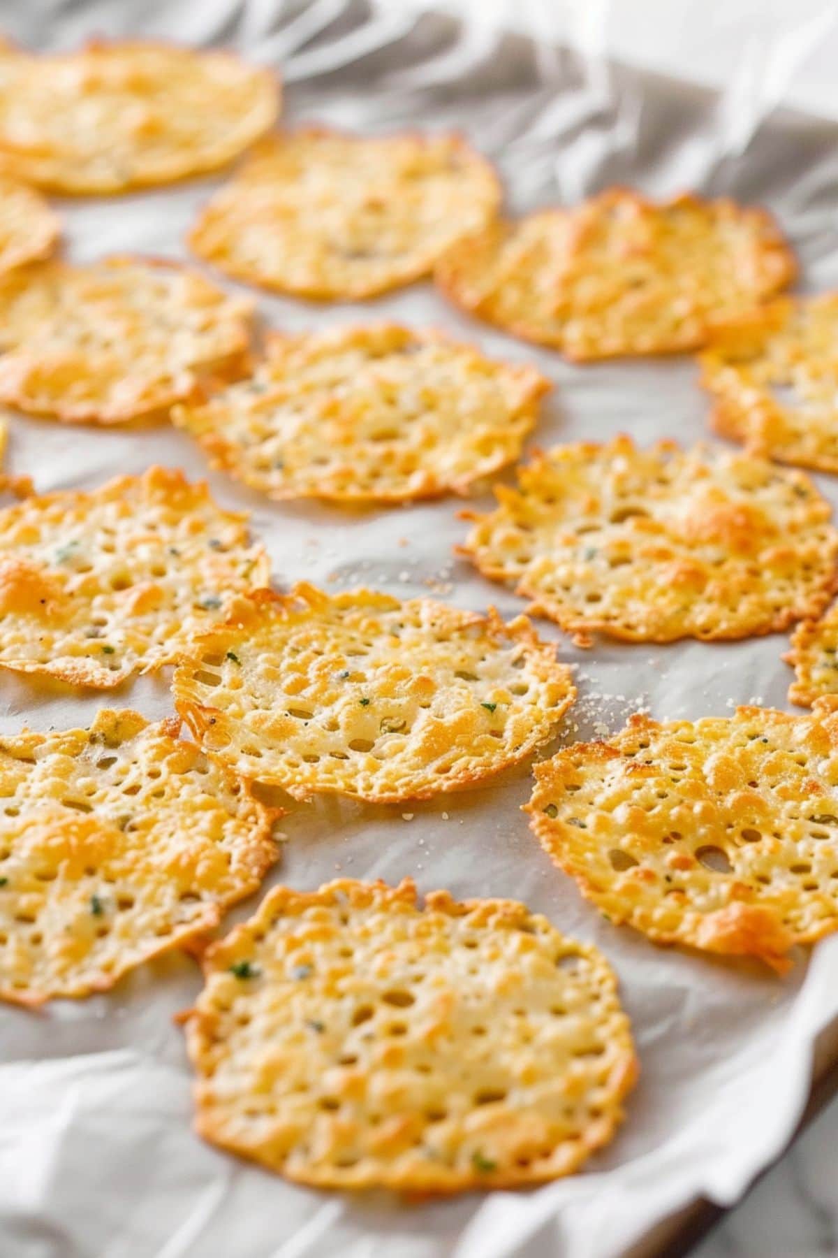 Crispy thin melted parmesan crisps on a baking sheet with parchment paper.