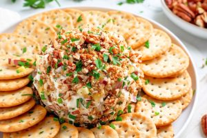 Pineapple cheese balls rolled in chopped pecans served in a platter of crackers in a large white plate.