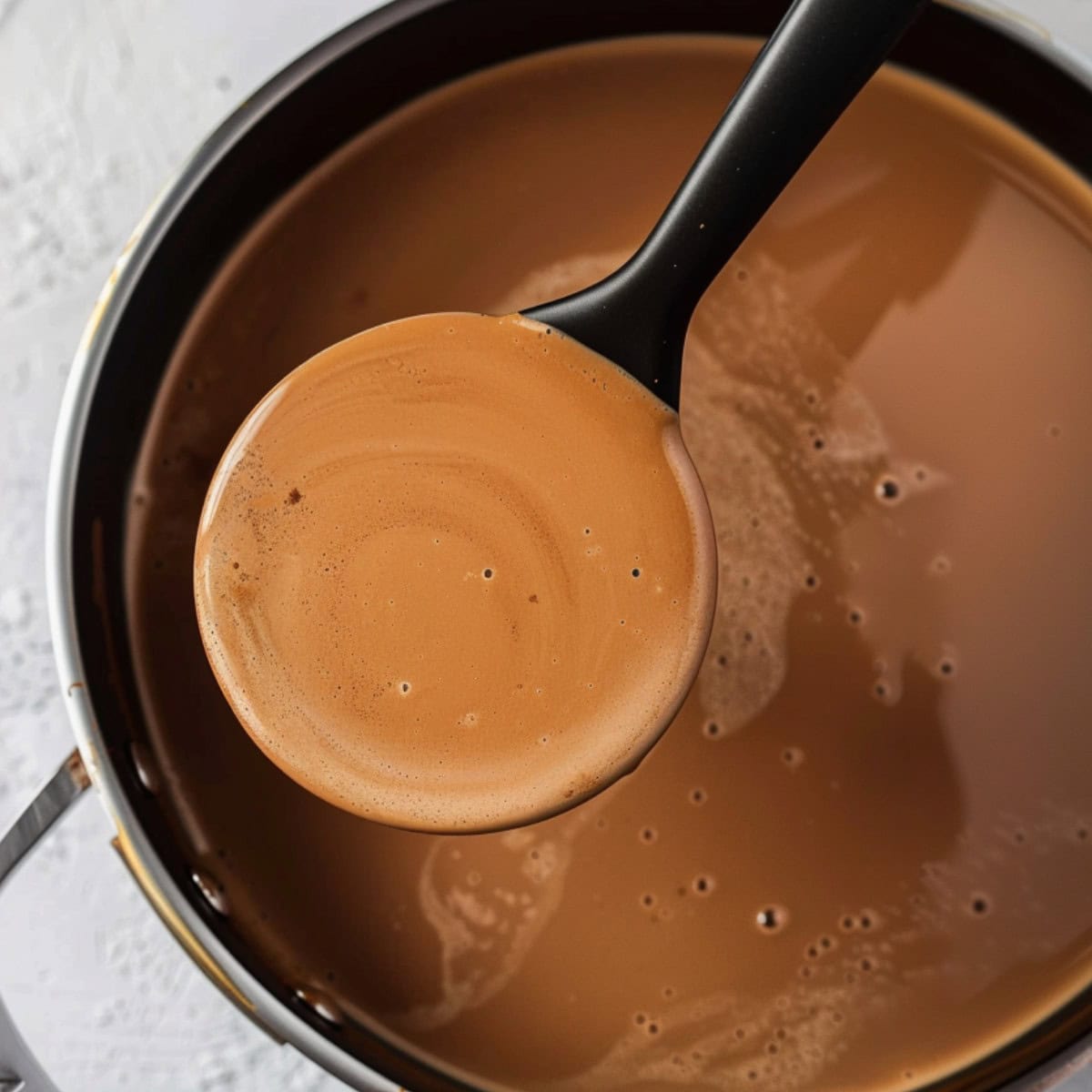 Soup ladle scooping a serving of creamy and chocolatey drink from a sauce pan. 