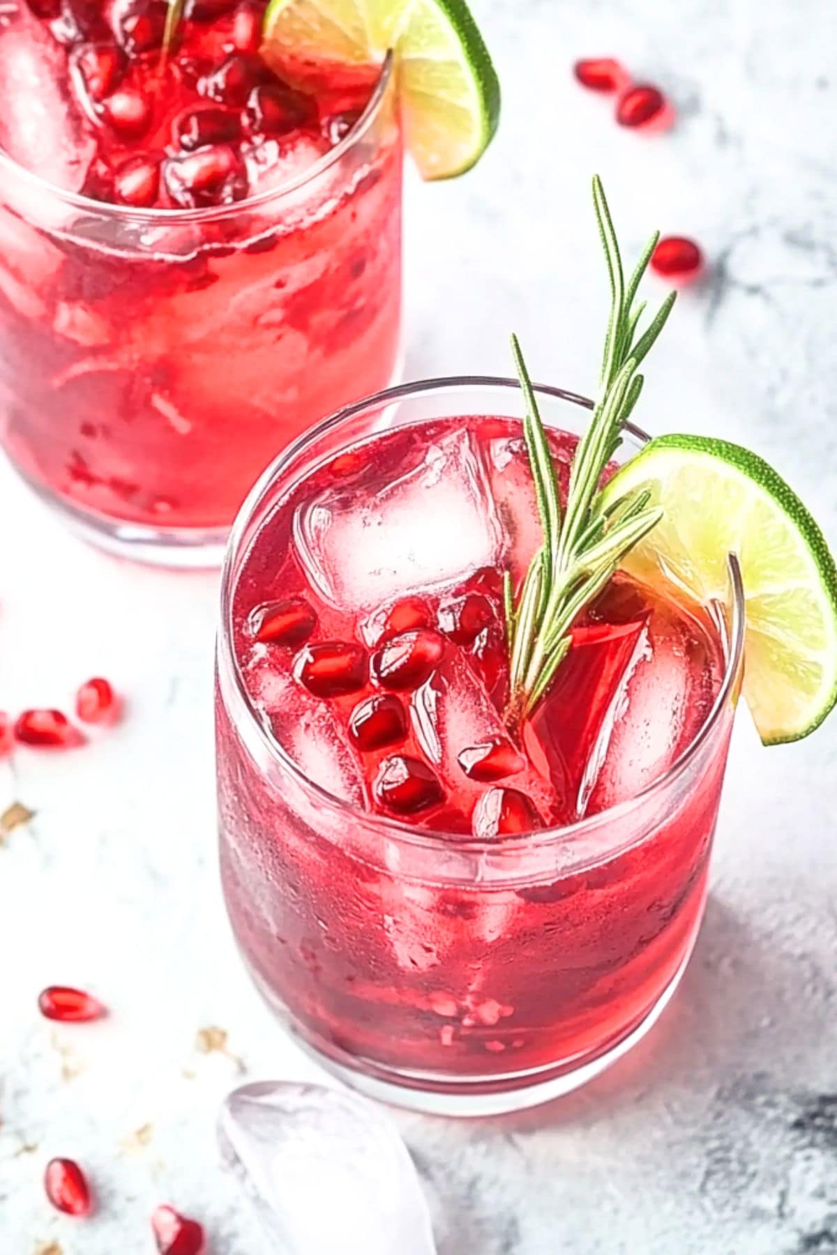 Top view of glasses filled with pomegranate mocktails, topped with pomegranate seeds, rosemary sprigs and lime wheels.