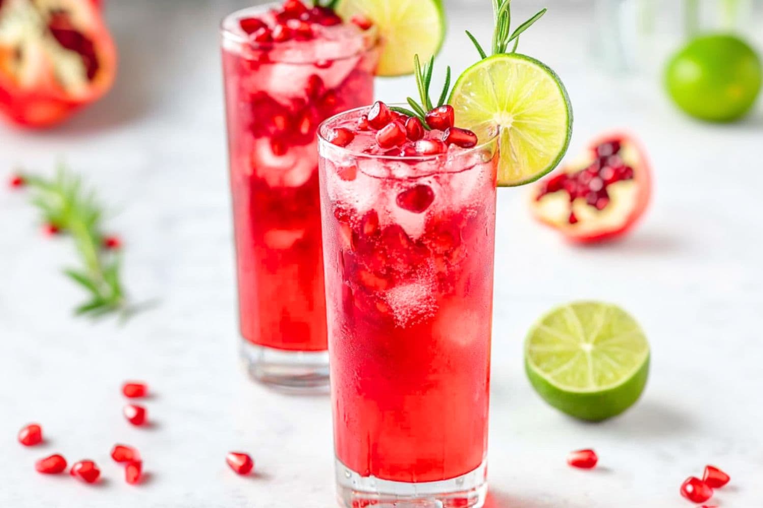 Two glasses of pomegranate sparkler mocktails served with ice, seeds and lime wheel.