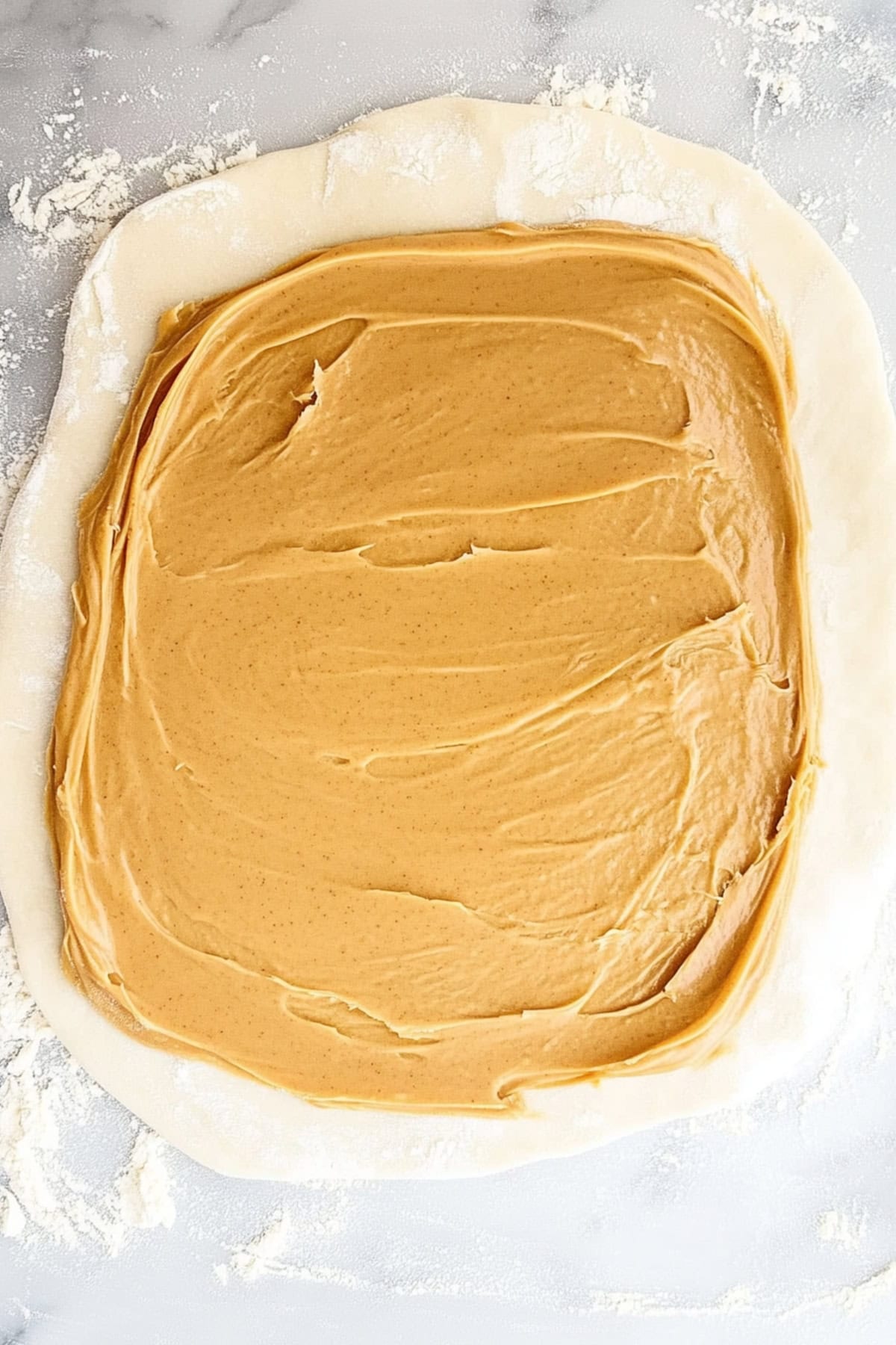 Potato candy with peanut butter being spread on top, on a white marble table