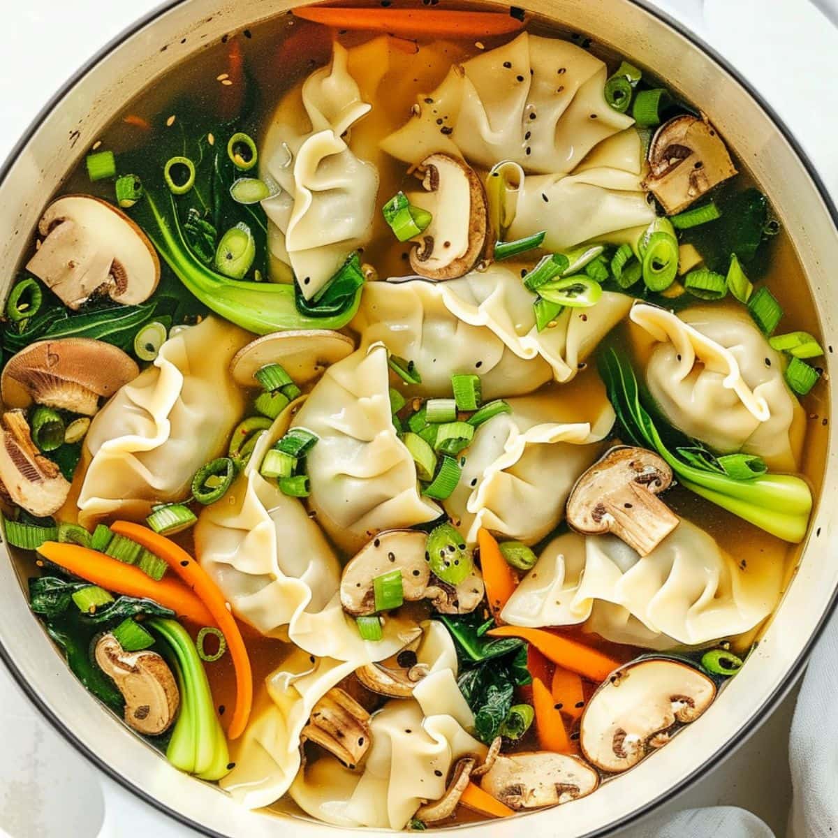 Potsticker soup in a pot with carrots, bok choy, green onion, and sliced mushroom