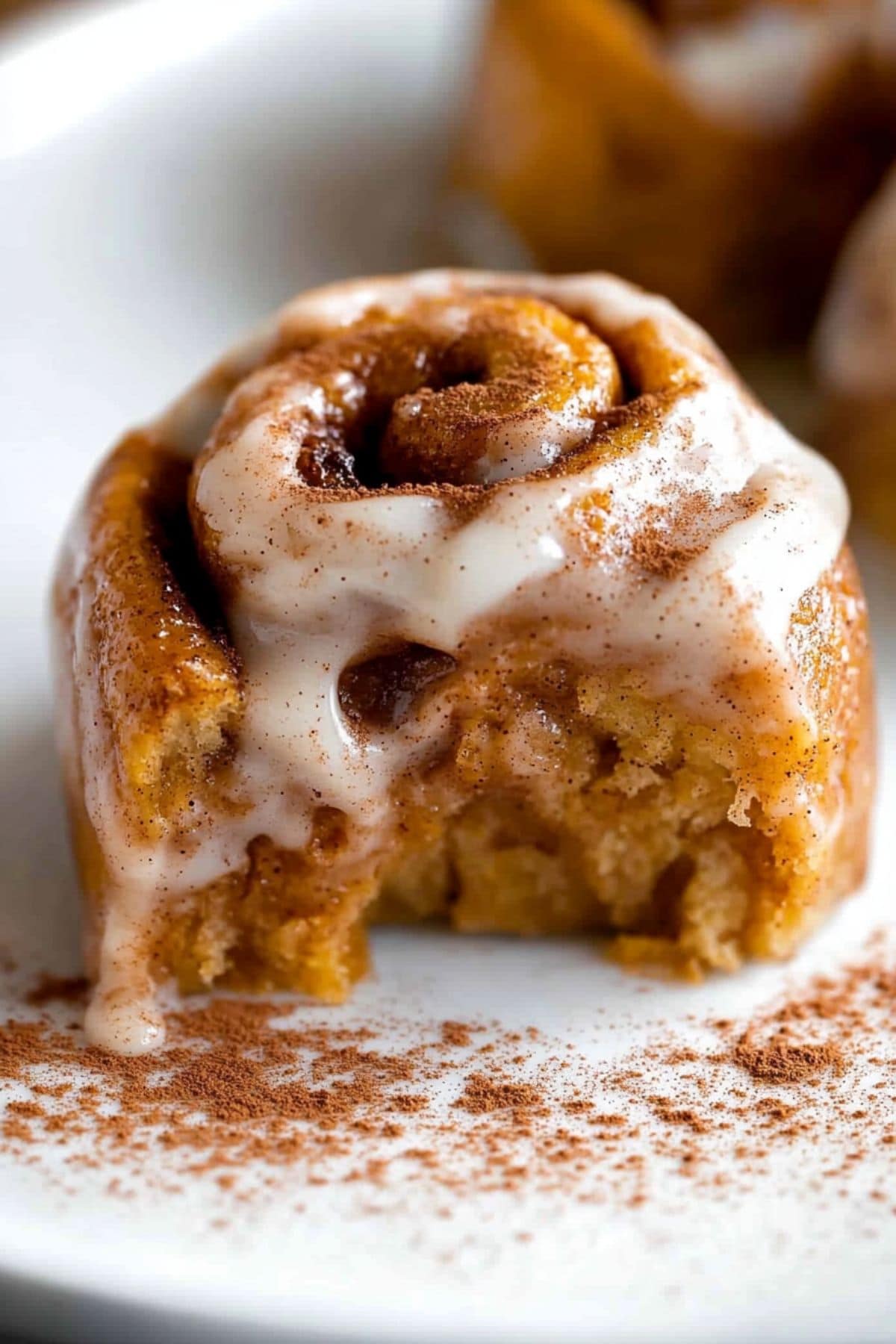 Pumpkin cinnamon roll sitting on a white surface dusted with cinnamon powder.