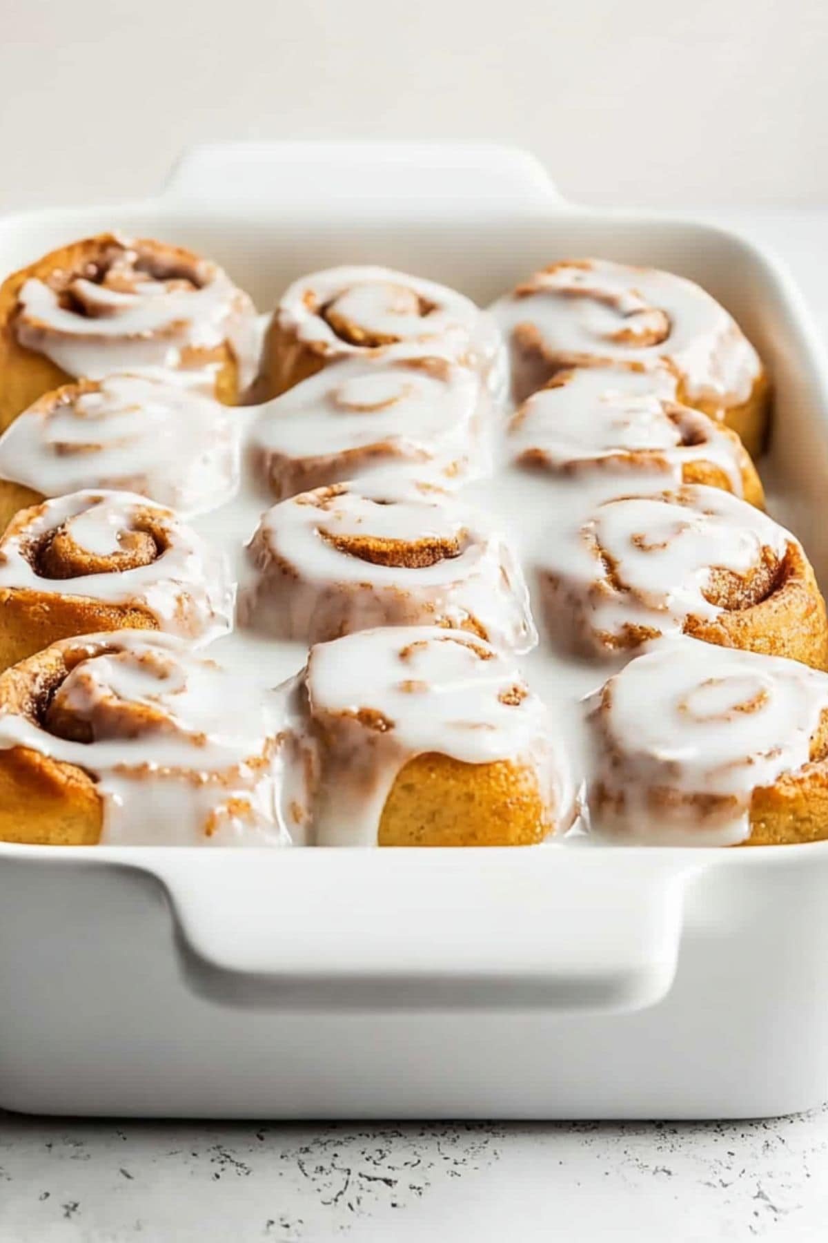 Rectangular white baking dish with cinnamon rolls covered with cream cheese frosting on top.