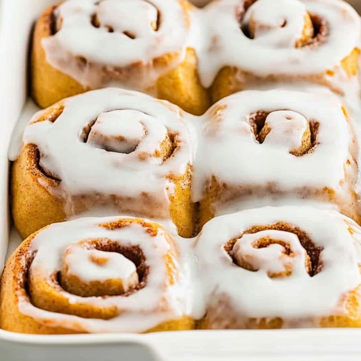 Pumpkin cinnamon rolls covered with sugar glaze baked in a rectangular baking dish.