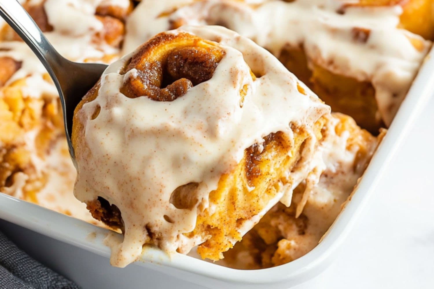 Pie ladle lifting a piece of cinnamon roll from the baking dish.