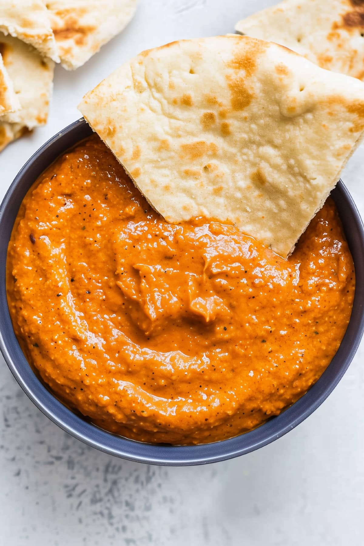 Close-up of roasted red pepper dip, smooth and velvety in texture, served with pita bread.