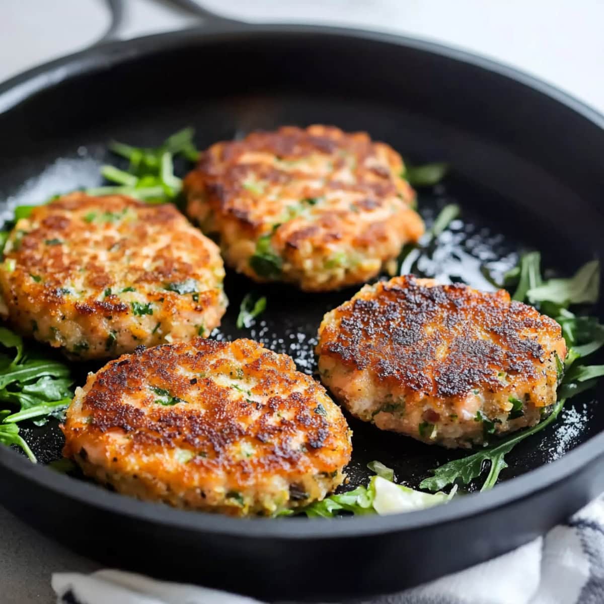 A skillet filled with salmon cakes on a white marble table.