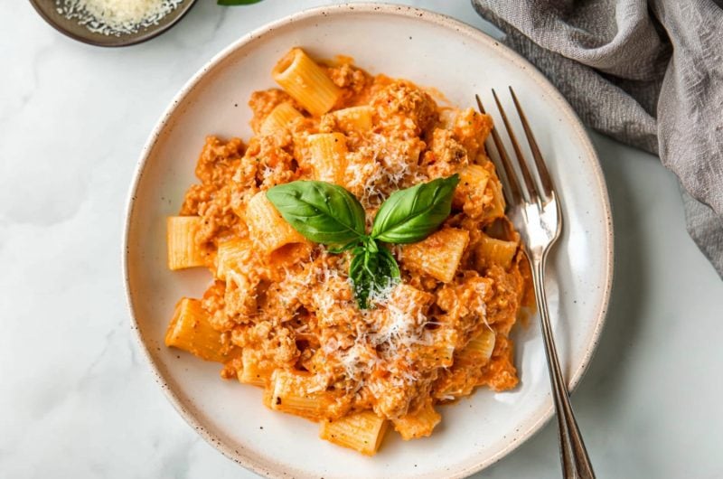 Sausage rigatoni in rich tomato sauce, garnished with basil and parmesan, fork on the side.