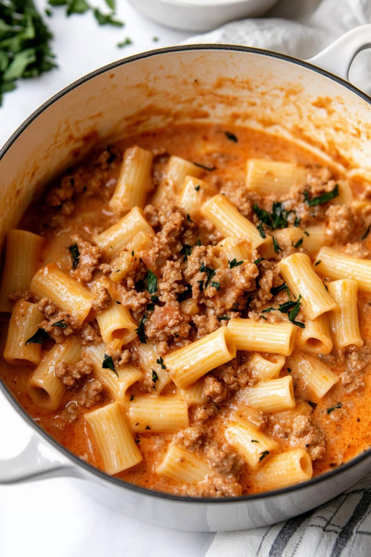 A deep pot of rigatoni pasta with ground beef and chopped parsley.