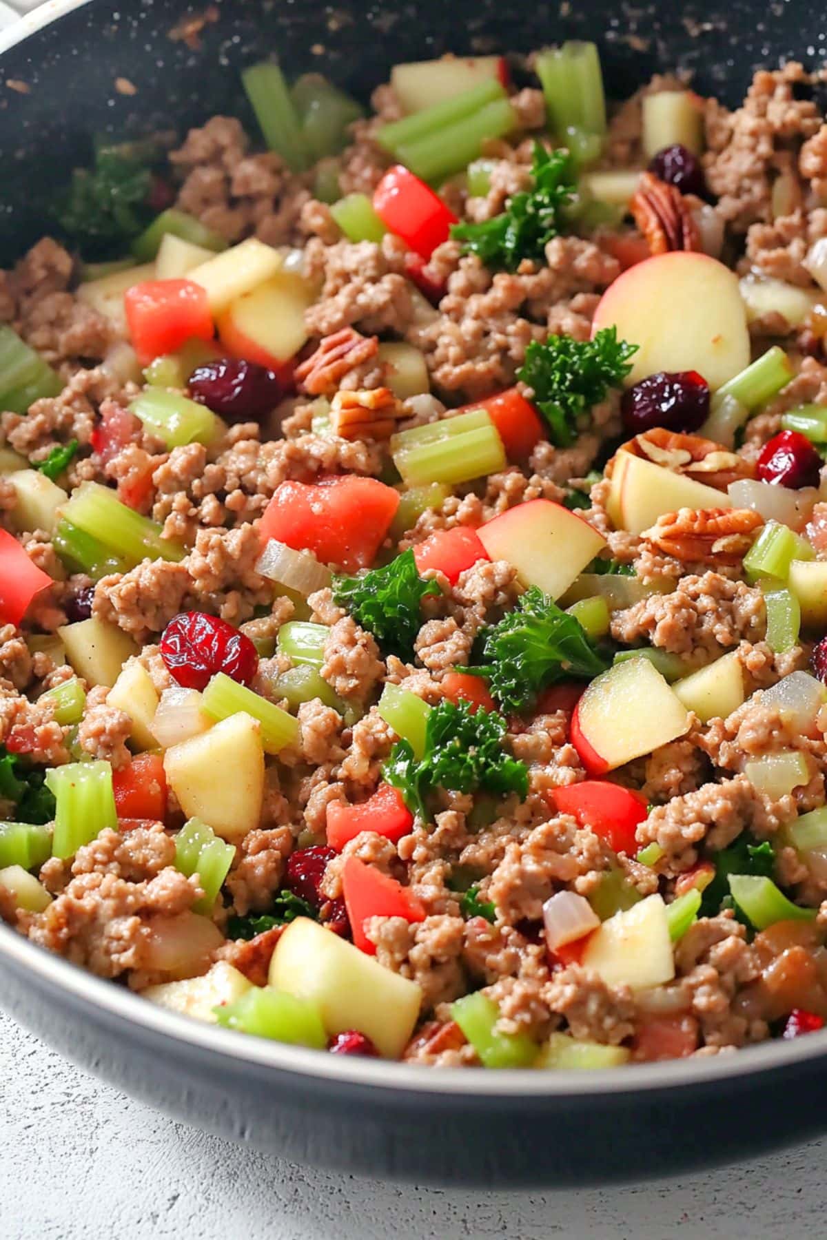 Sausage with chopped onion, celery, red bell pepper, and apple in a pan. 