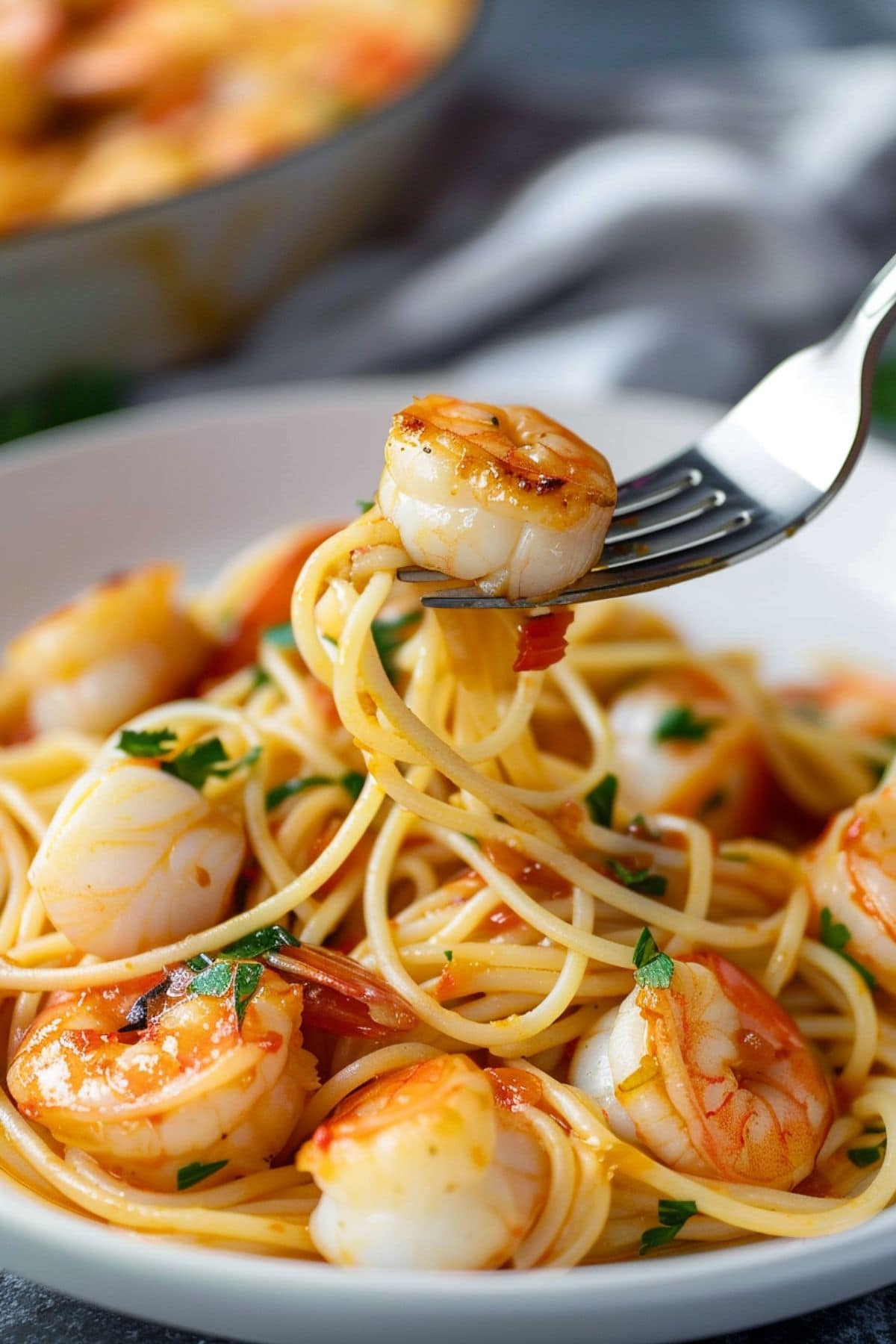 Fork with a piece of scallop from a serving of scallop and shrimp pasta in a plate.