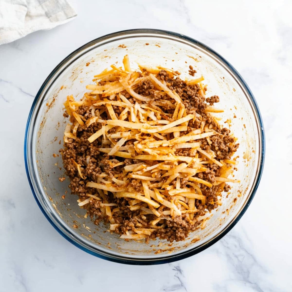 A glass bowl of shredded hashbrowns and cooked ground beef, top view