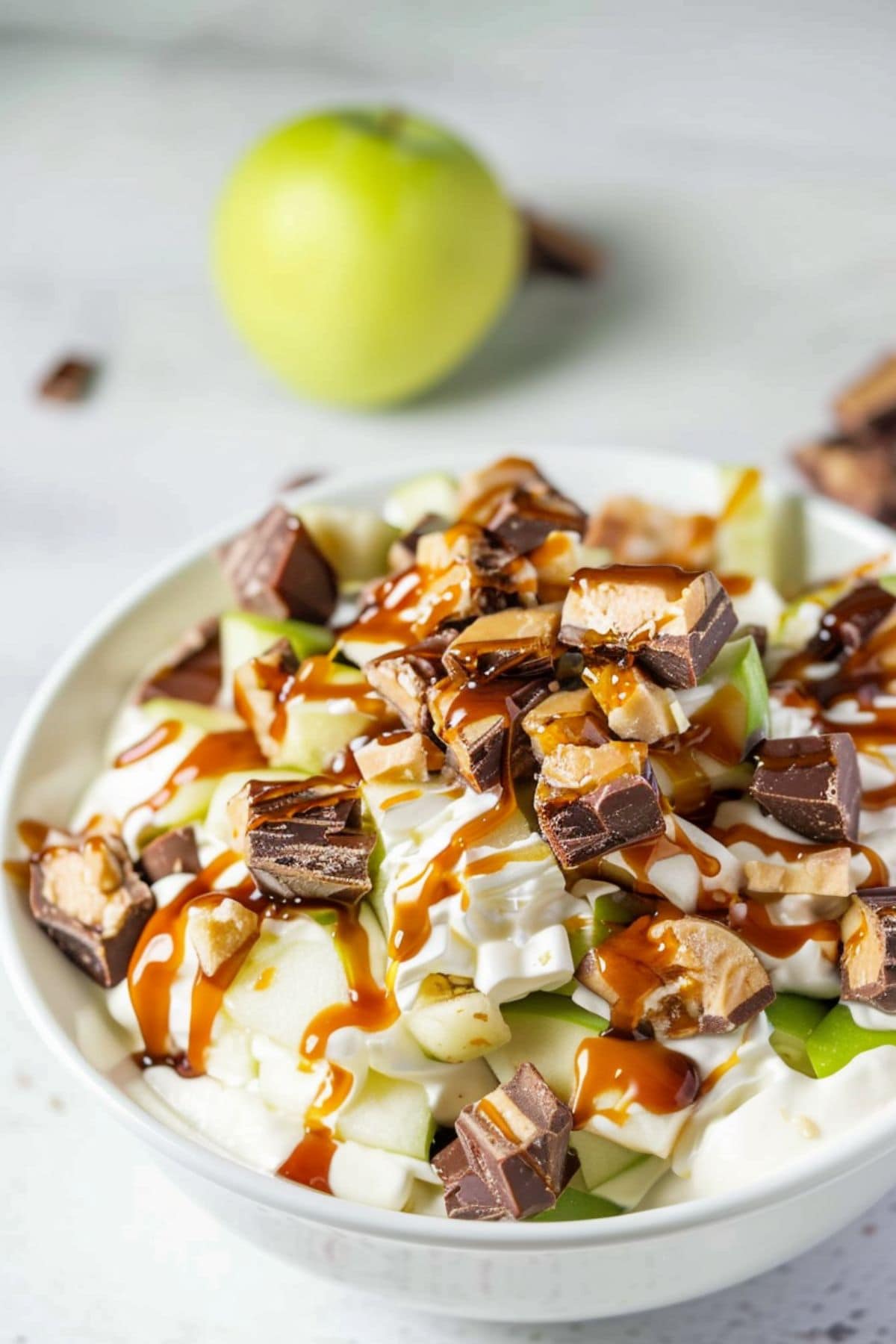 White bowl with a serving of Snickers salad made with chopped Snickers candy and green apples tossed with creamy pudding.