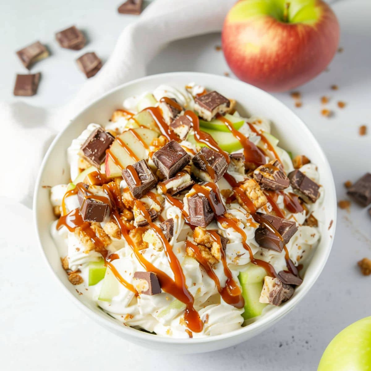 Snickers salad with chopped apples and Snickers in a white bowl.