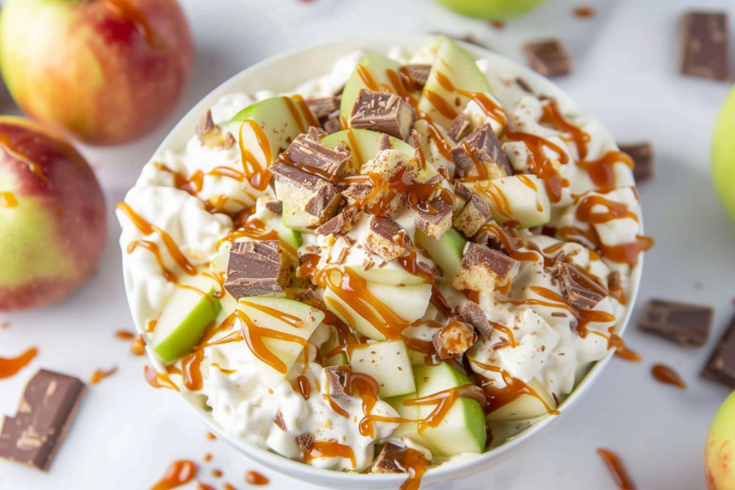 Snickers salad with mix of chopped green apples and chopped Snickers candy with creamy whipped cream pudding served in a white bowl.