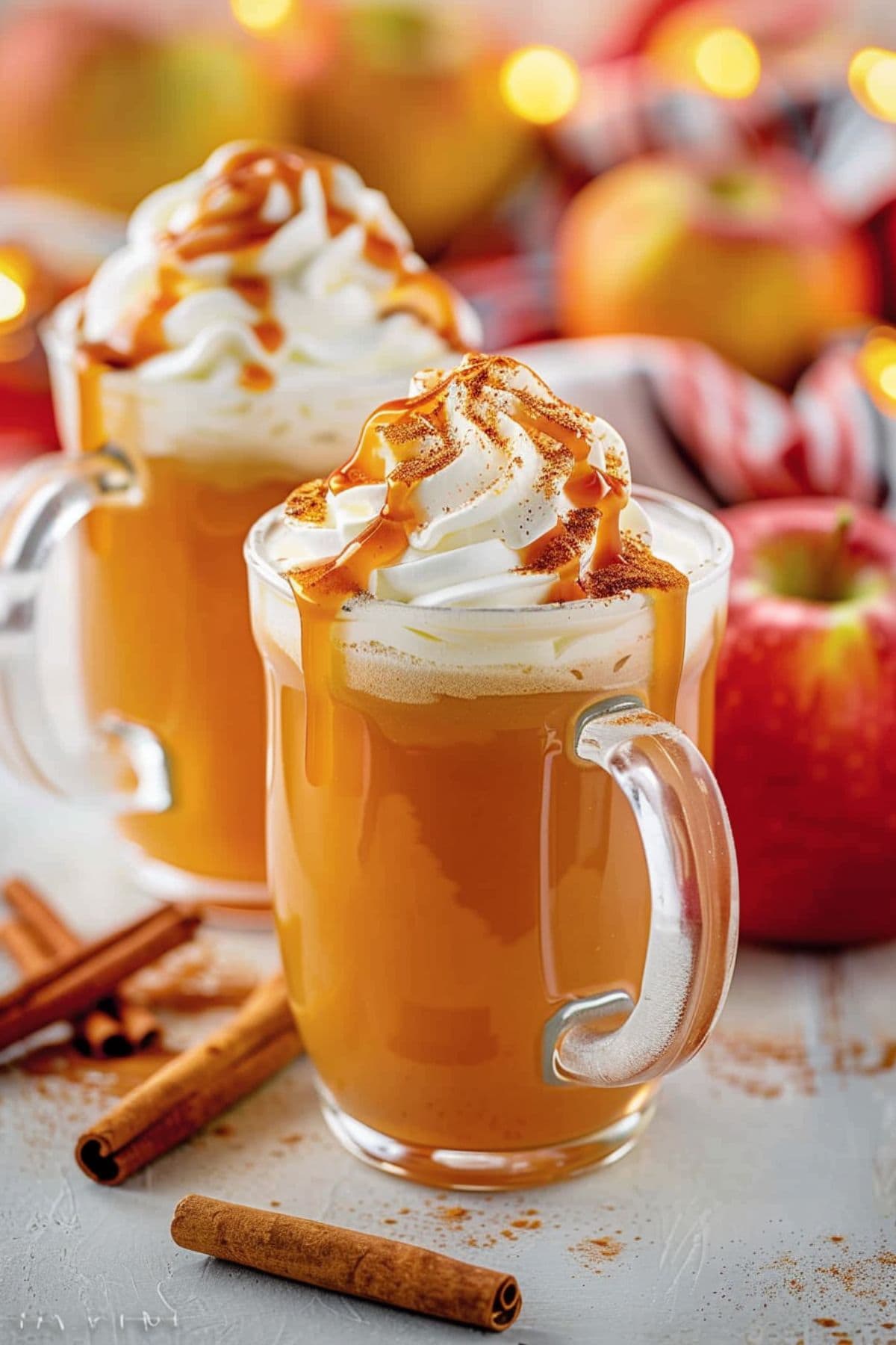 Two glass servings of caramel apple cider with whipped cream served in glass mug.