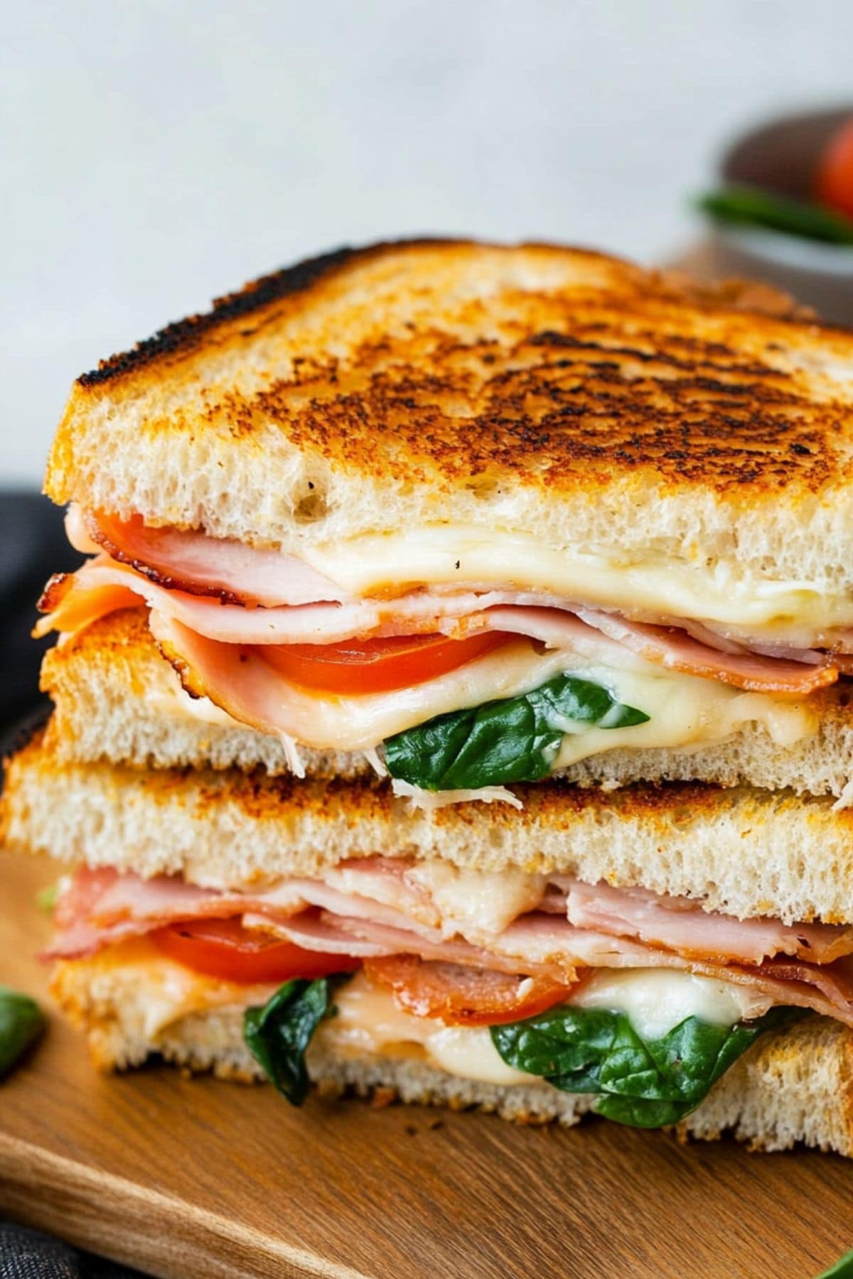 Toasted turkey melt sandwich with tomato, turkey, bacon, spinach, and cheese cut in half on a cutting board.