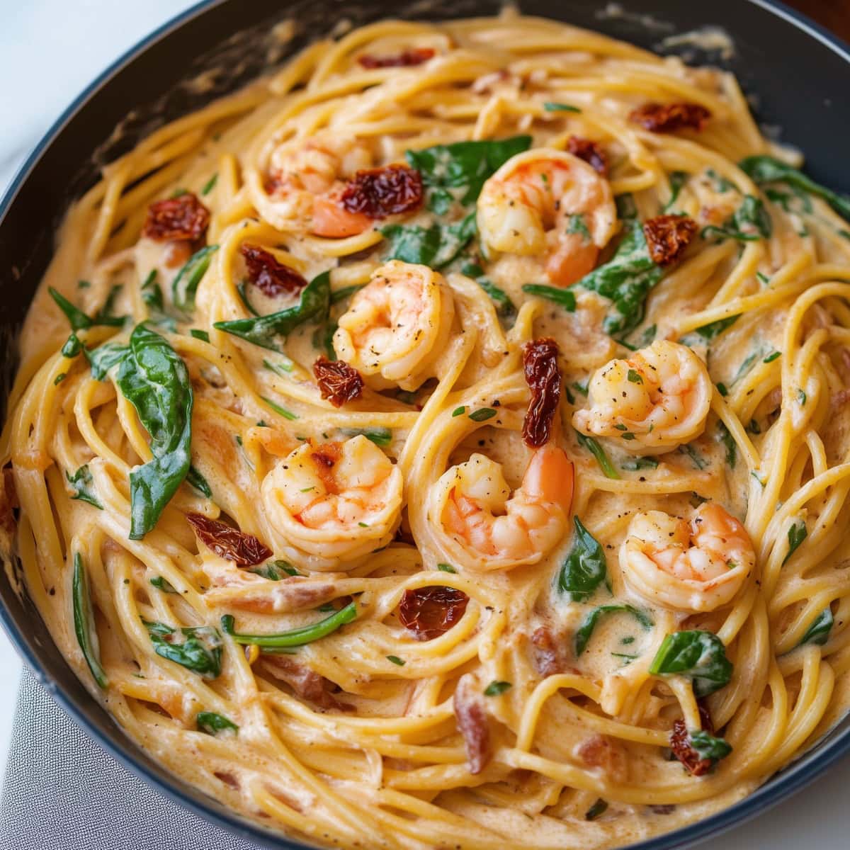 Close-up of creamy tuscan shrimp pasta in a skillet.