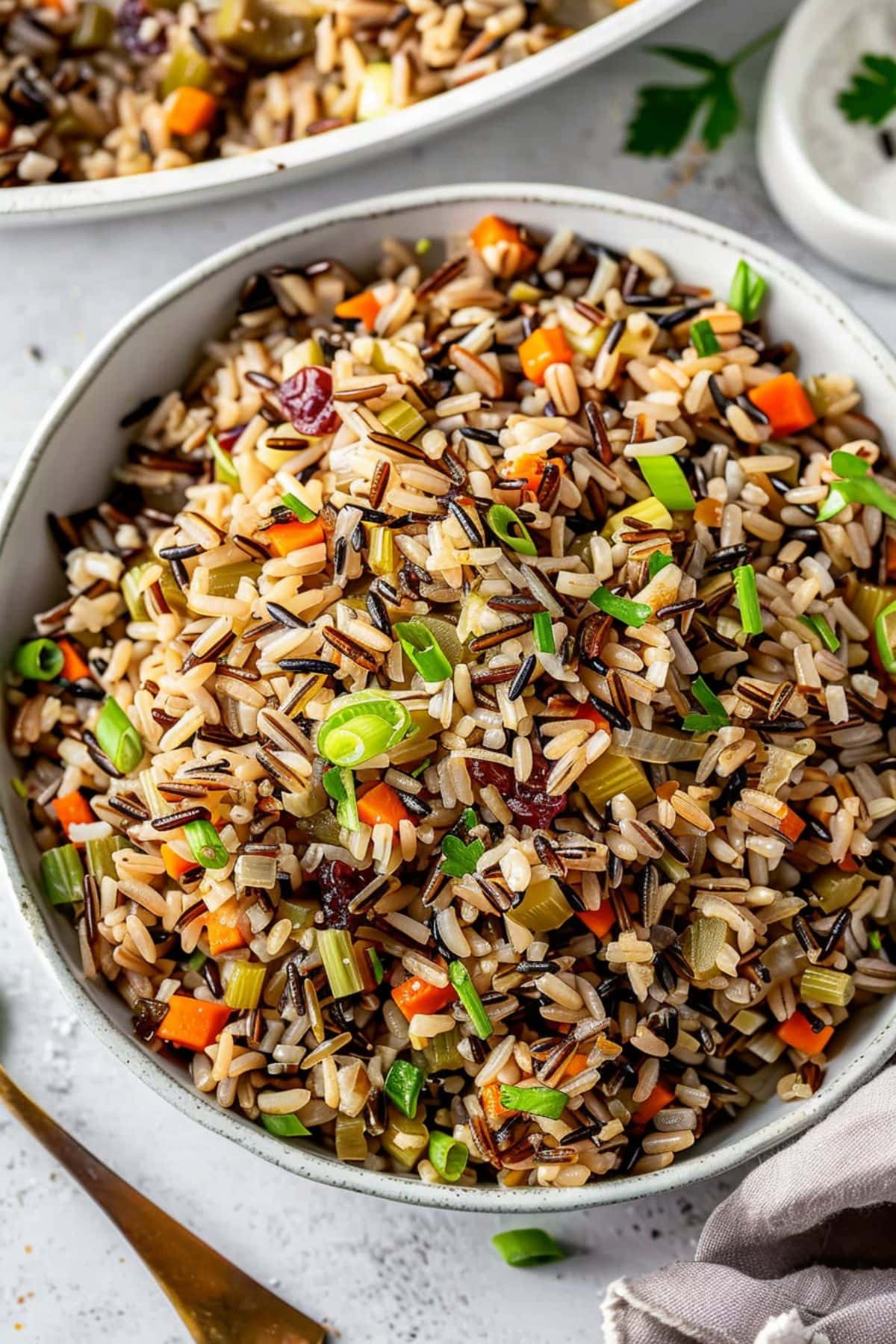 Wild rice with cranberries, chopped nuts, carrots and green onion served in a white bowl.