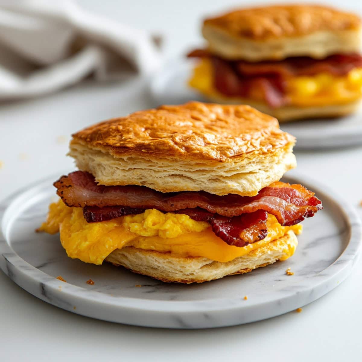 Biscuit breakfast served in a white plate with scrambled eggs a nd bacon filling. 