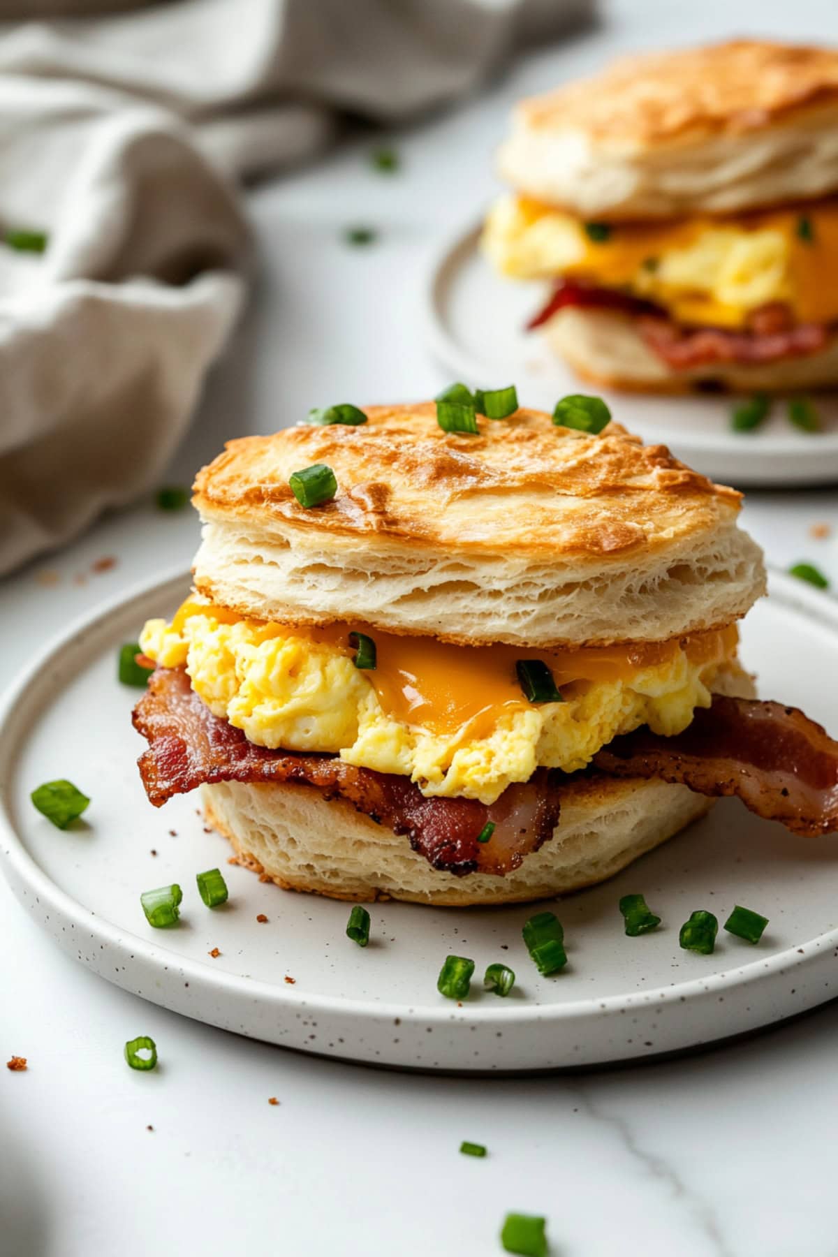 Biscuit breakfast sandwiches with scrambled egg and bacon filling served in a white plate.