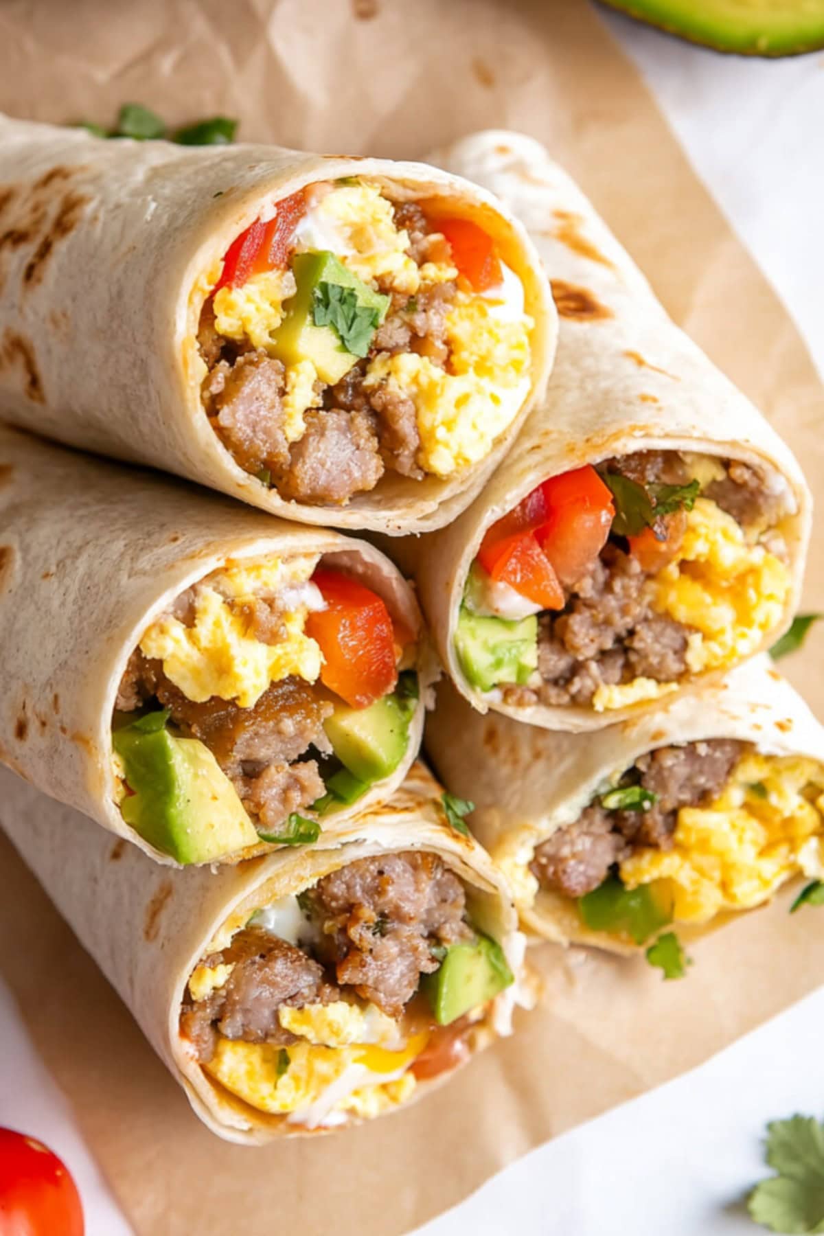 Loaded breakfast burritos with egg, avocados, tomatoes and sausage, garnished with cilantro.