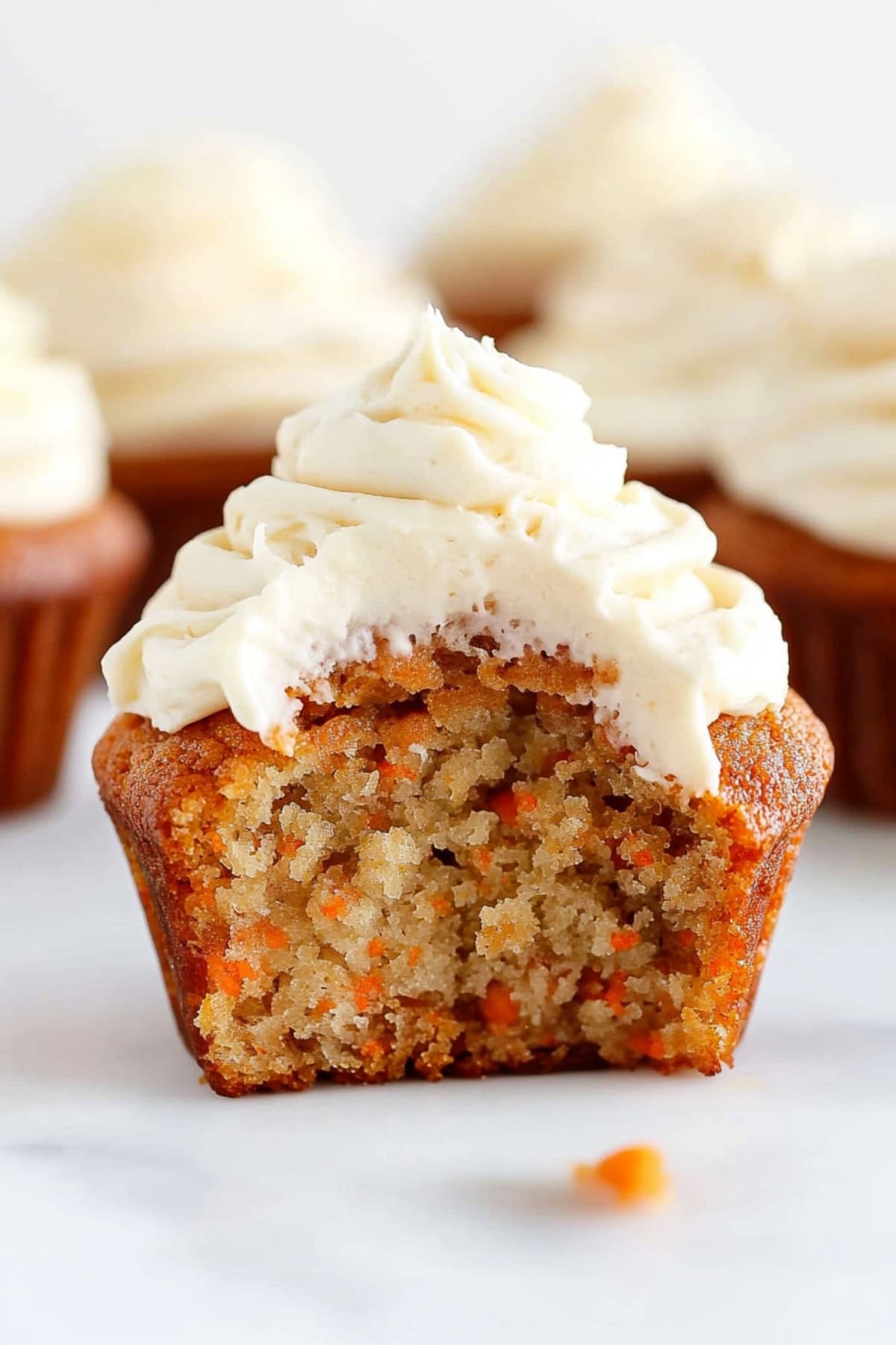 Carrot cupcake topped with frosting cut in half.