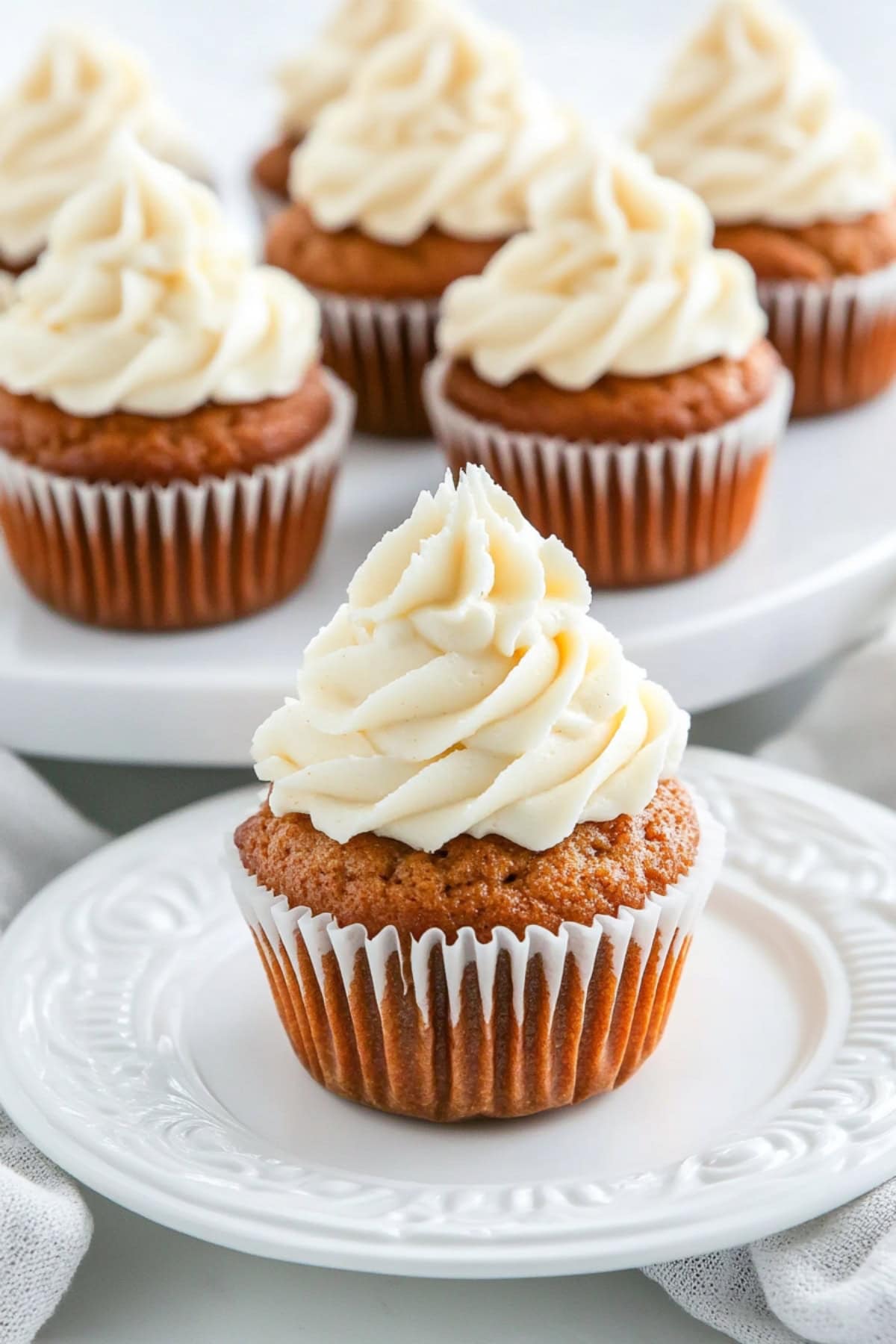 Carrot cupcake wit cream frosting served in a plate with the rest of the cupcakes in the background sitting in a cake tray.