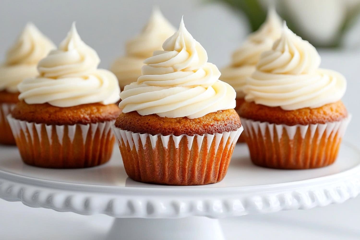 Bunch of carrot cupcake s with frosting sitting on top of a white cake tray.