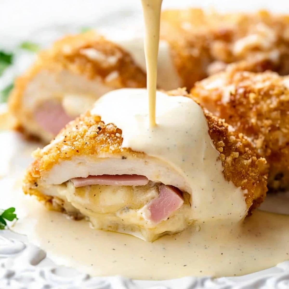 A creamy sauce being poured into a piece of chicken cordon bleu