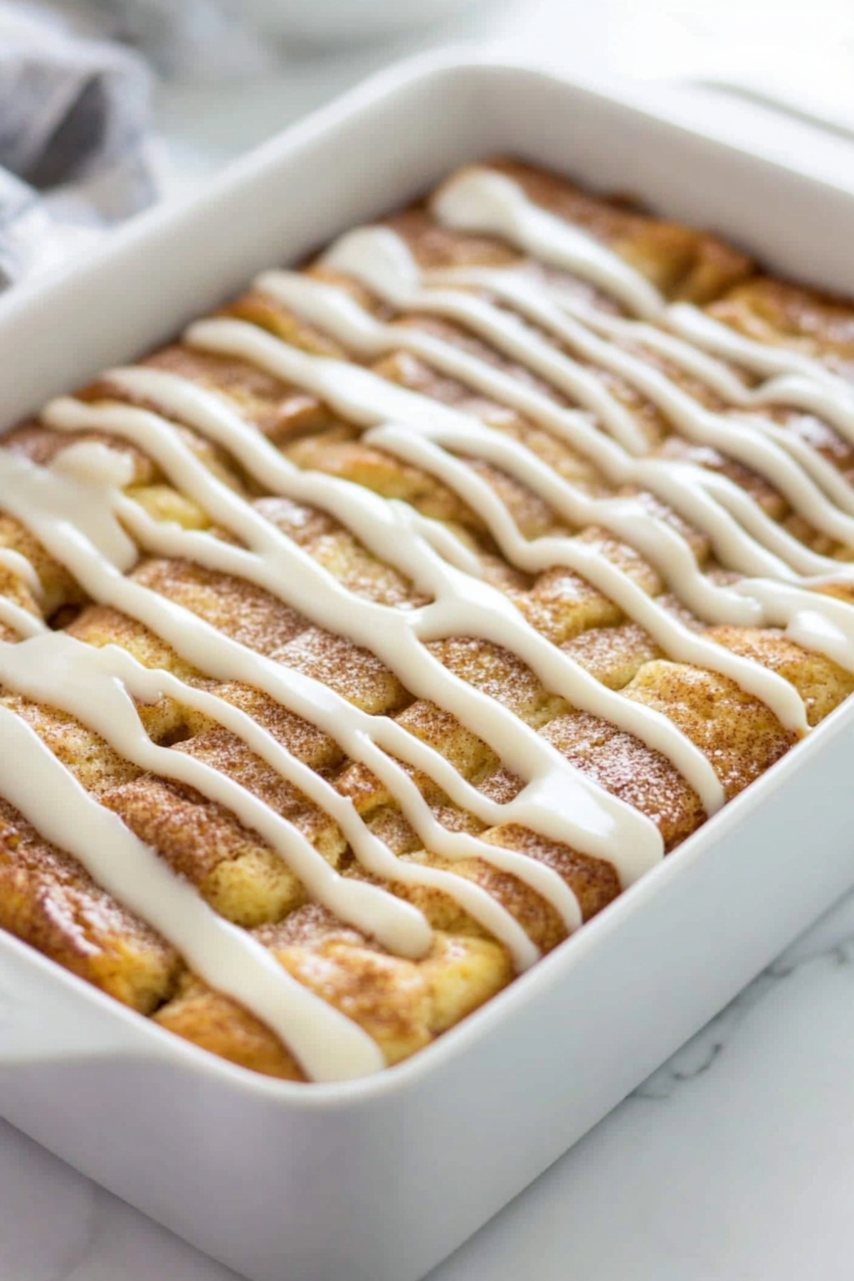 Cinnamon roll coffee cake in a baking dish drizzled with white glaze on top.