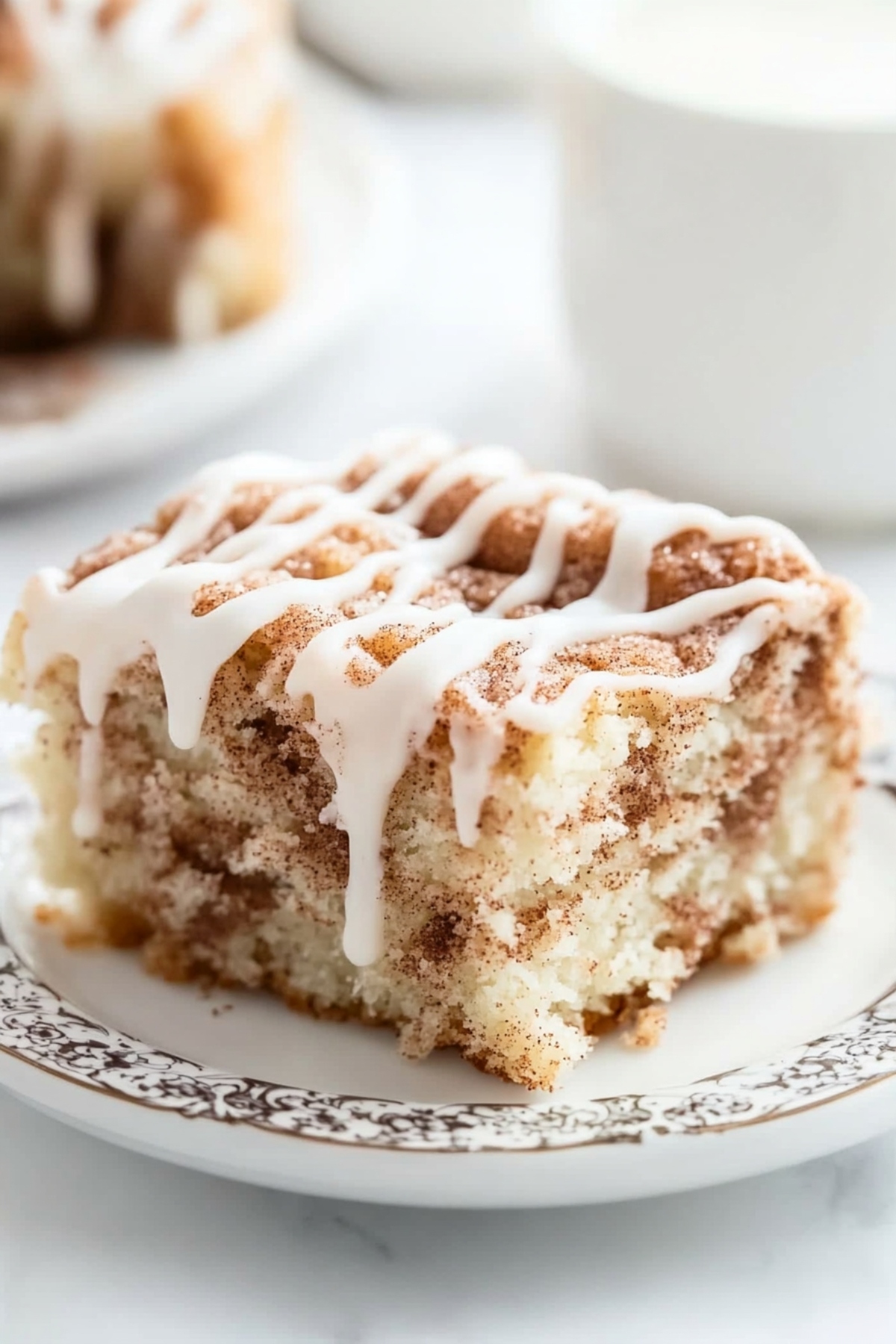 Cinnamon roll cake square slice served in a white plate drizzled with sugar glaze on top.