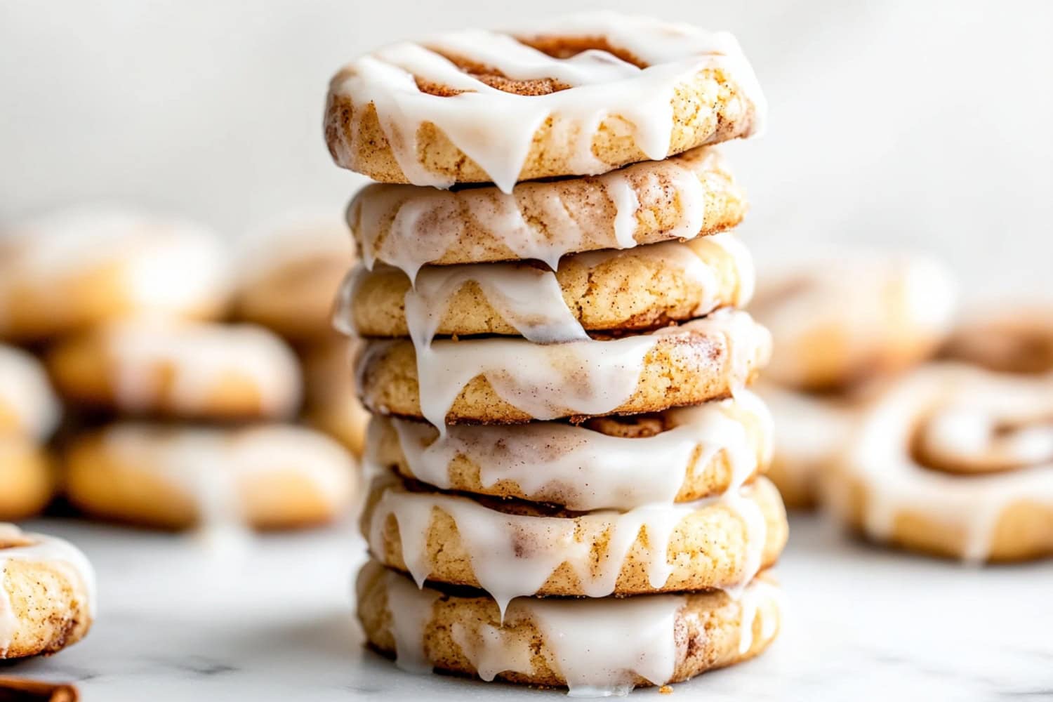 A stack of cinnamon roll cookies drizzled with glaze sitting on a marble table.