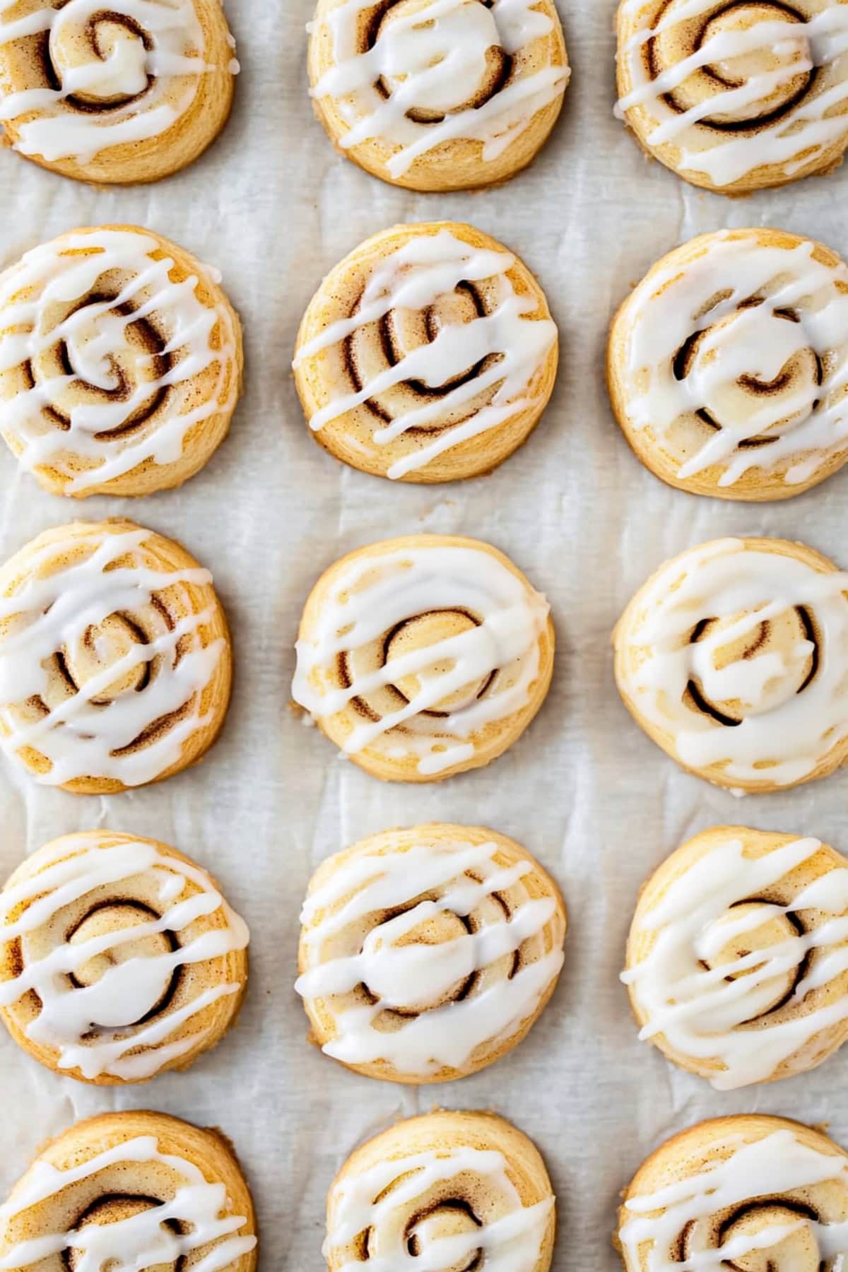 An overhead view of cinnamon roll cookies with glaze on parchment paper.