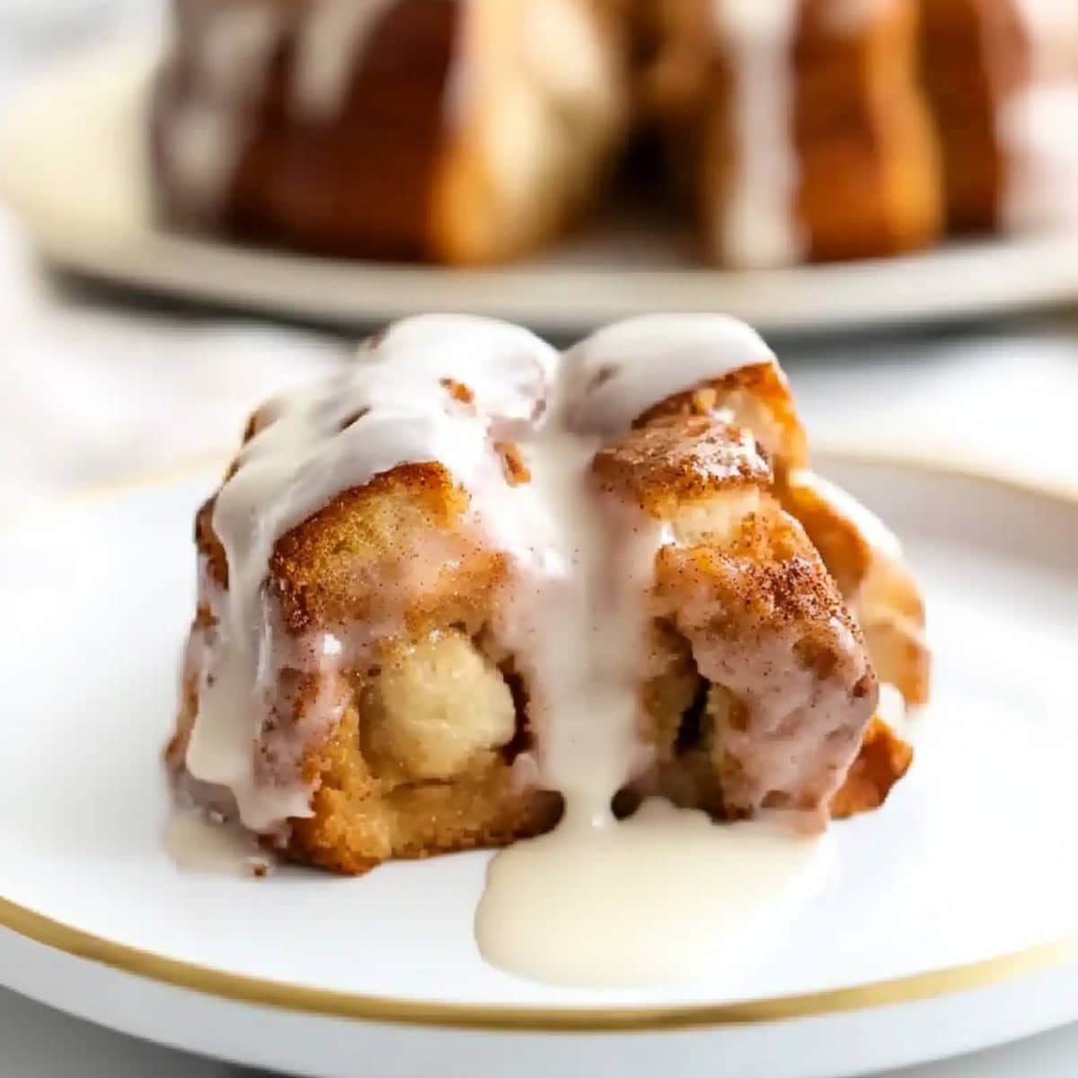 A piece of cinnamon roll monkey bread with creamy glaze on a plate.