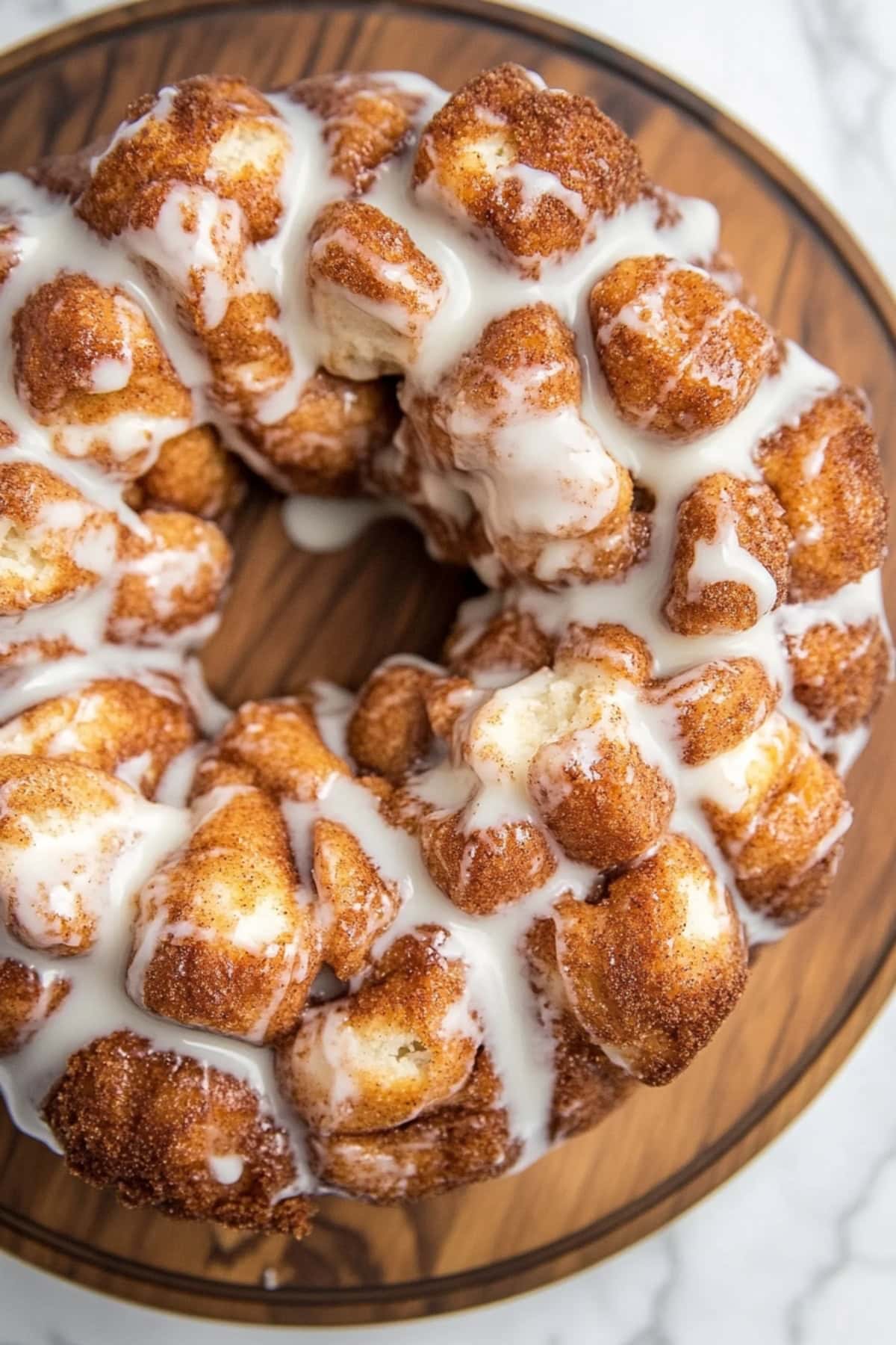 A wooden plate of cinnamon roll monkey bread with icing.