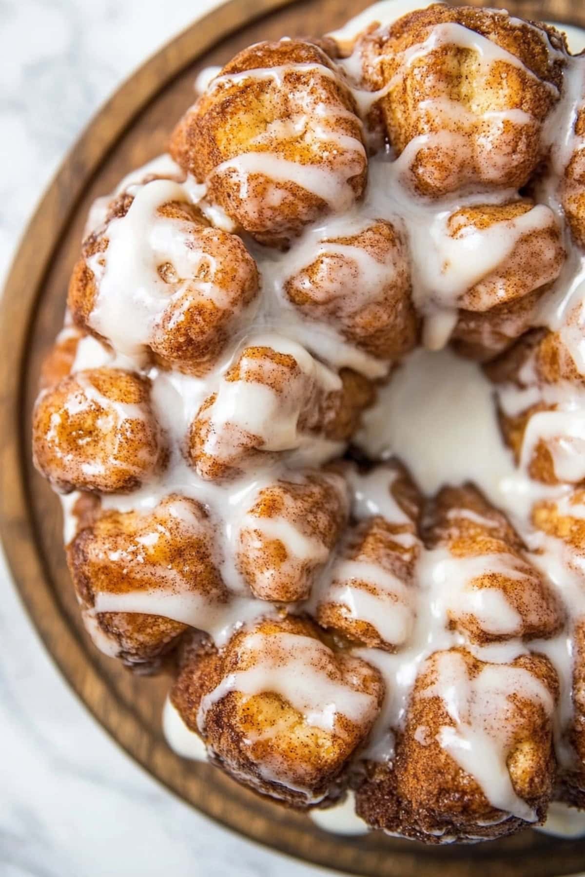 Golden-brown cinnamon roll monkey bread with glaze in a wooden plate.