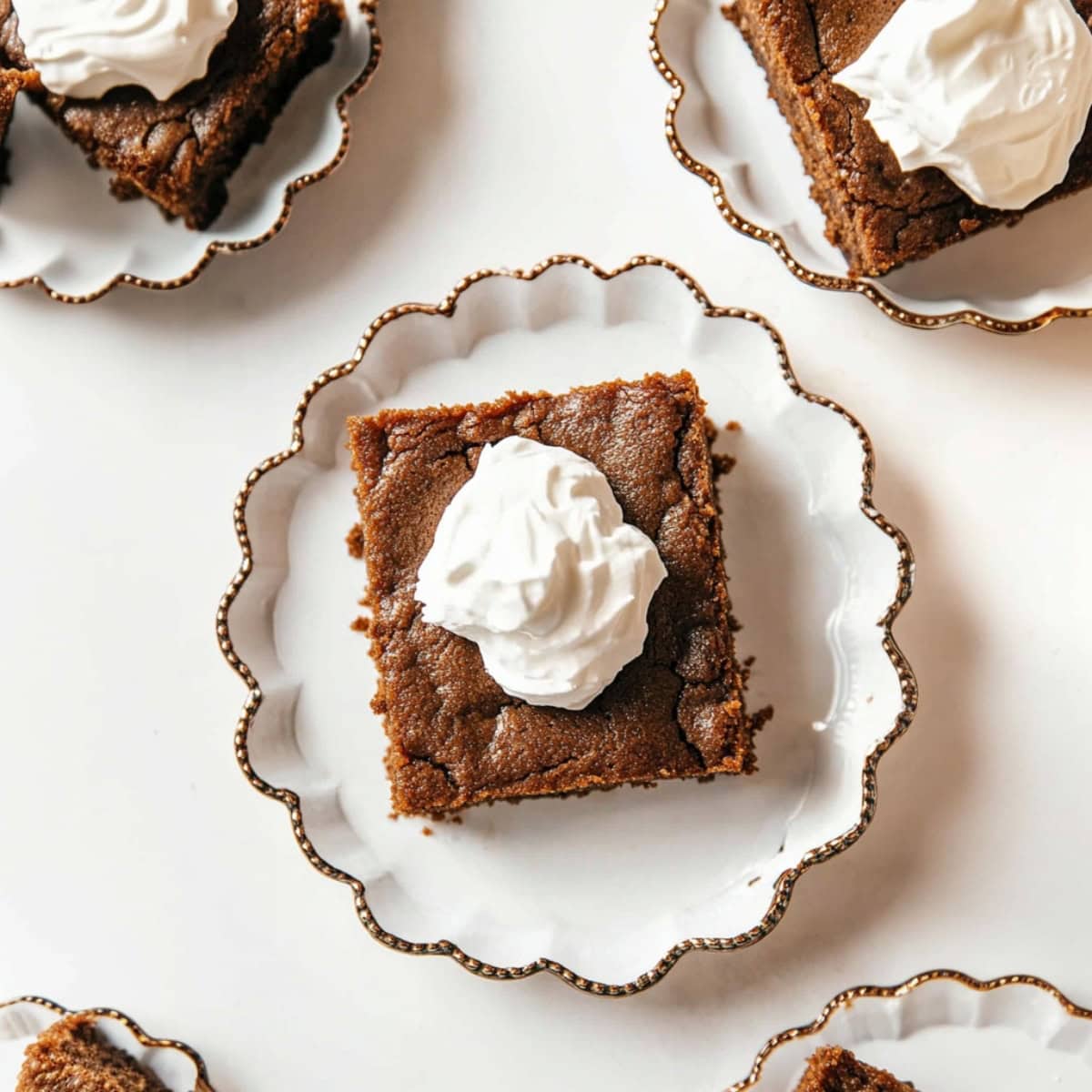 An overhead of gingerbread cake with whipped cream in an elegant plate.