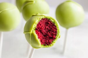 Bitten red velvet cake pops on stick coated with green shell.