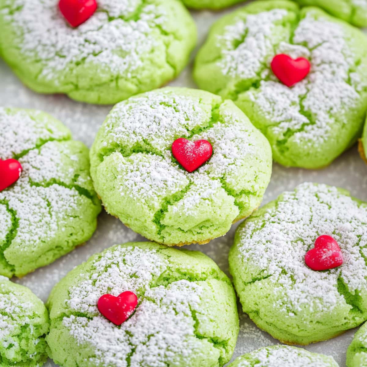 Bunch of Grinch cookies decorated with a heart shape candy sprinkle dusted with powdered sugar.