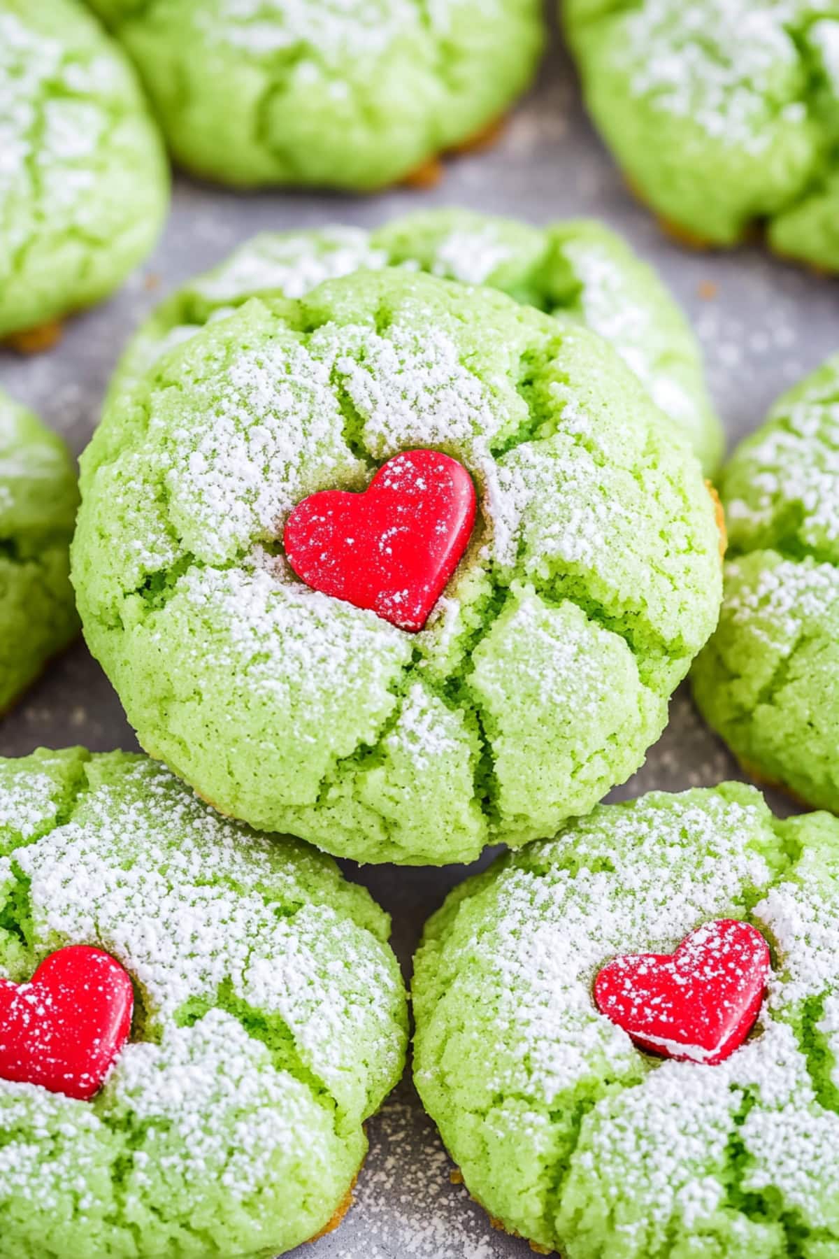 Bunch of green colored cookies decorated with heart shaped candy in the middle.