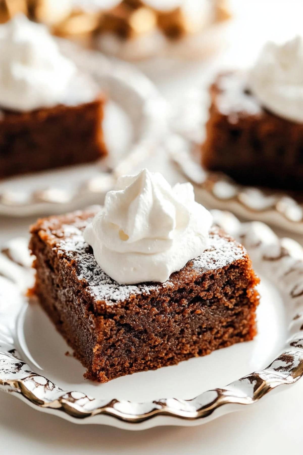 A slice of moist gingerbread cake topped with a dollop of whipped cream and a dusting powdered sugar.