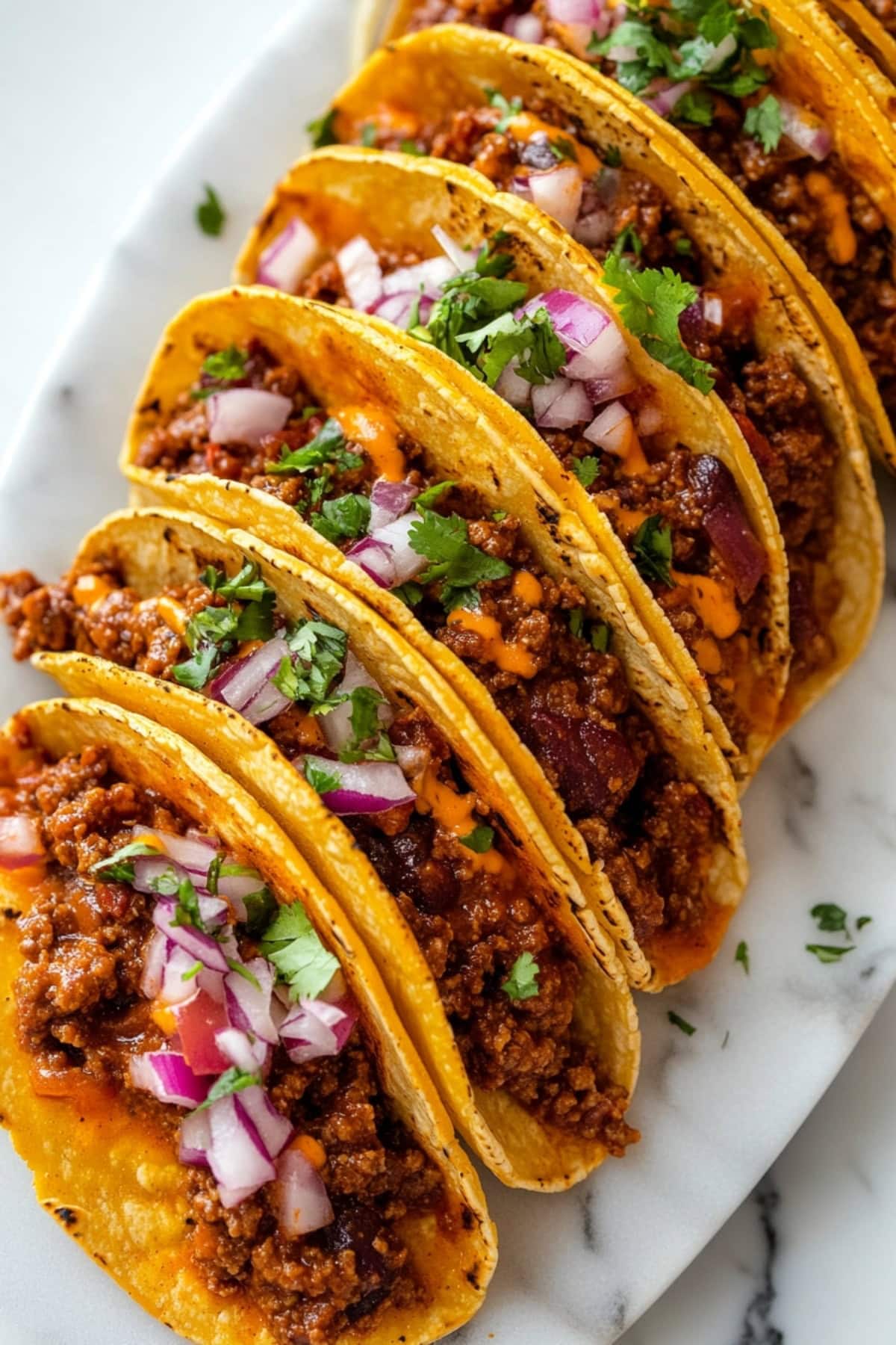 A plate of leftover sloppy joe tacos with soft tortillas filled with seasoned beef, melted cheese and diced onions.