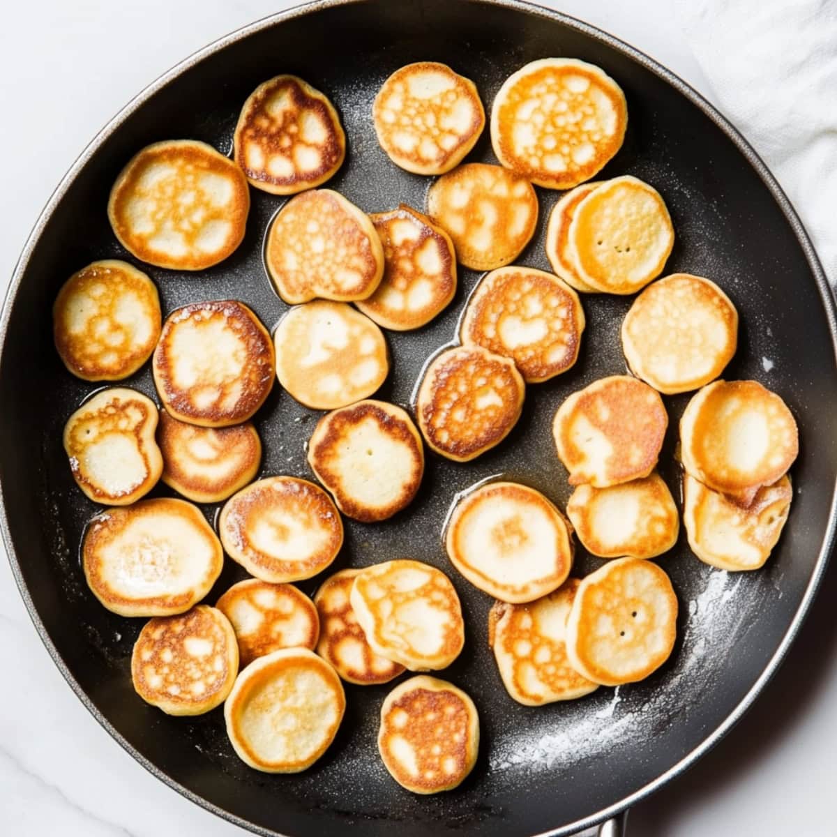 An overhead view of mini pancakes in a skillet.