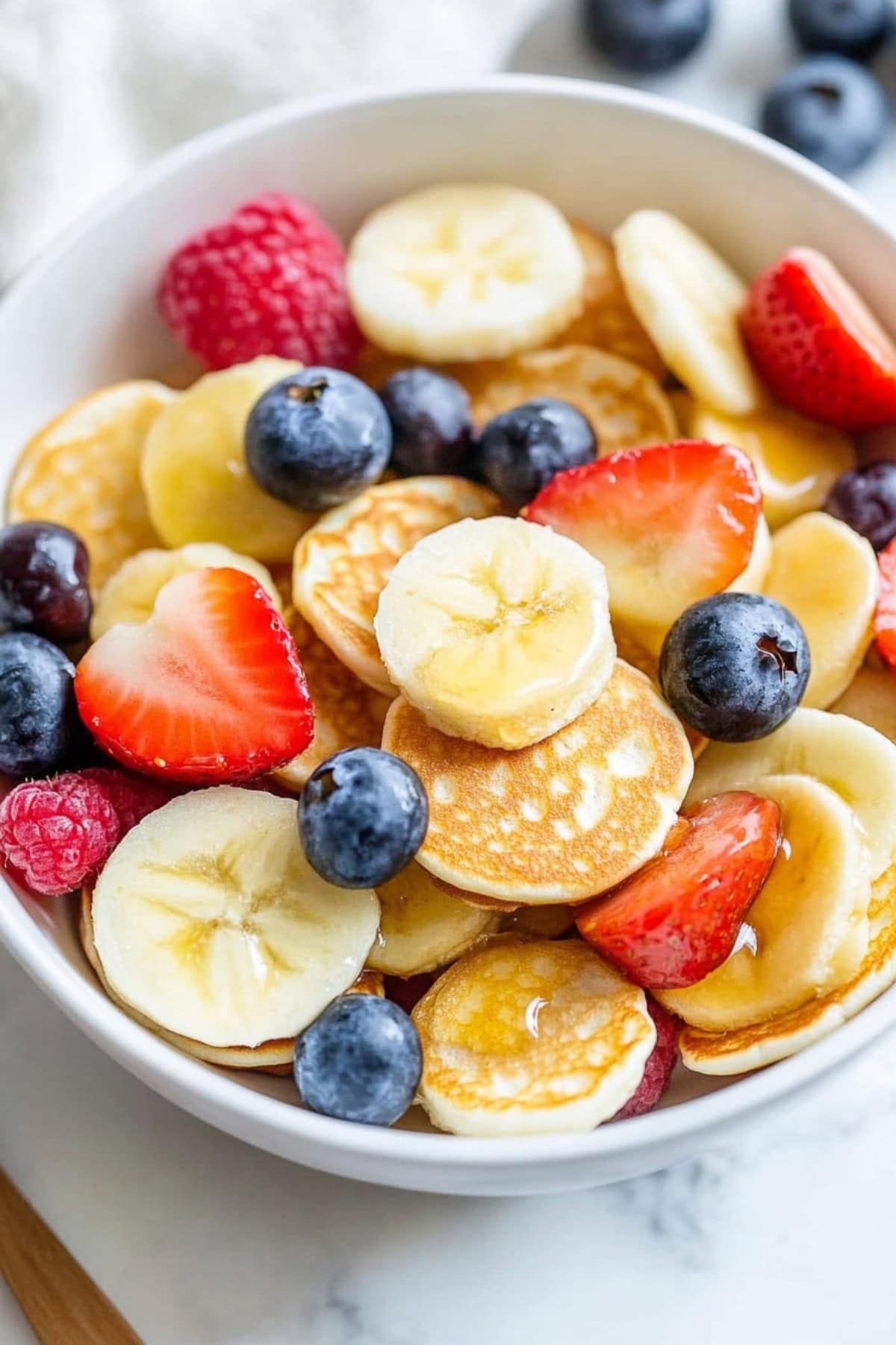 Homemade mini pancake cereal with berries and bananas in a bowl.