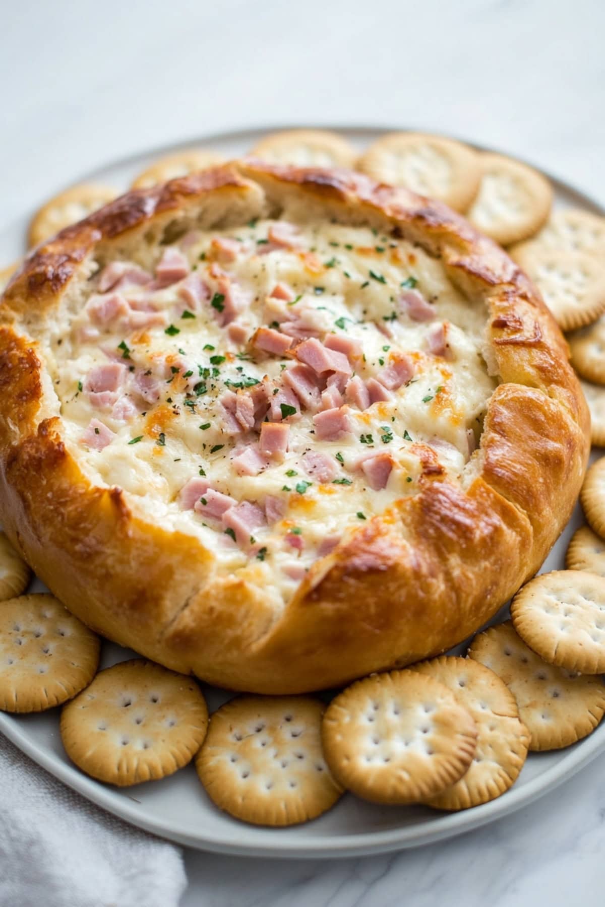 Hot cream cheese and sour cream dip with ham and green onions served inside a large bread loaf with crackers on the side