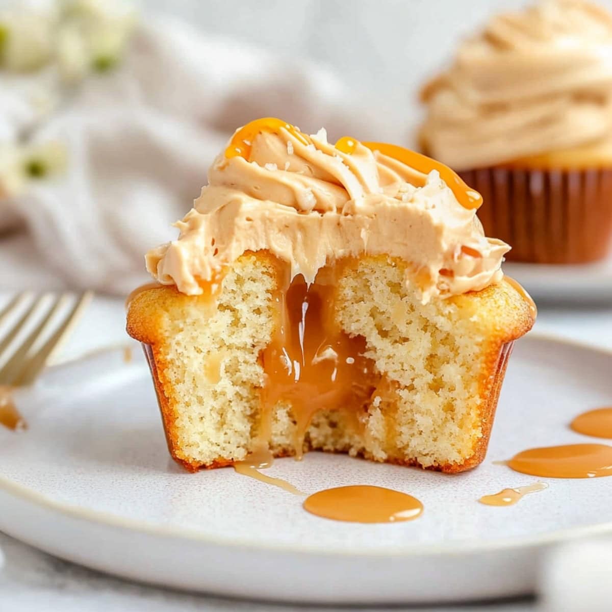 Halved cupcake filled with caramel sauce, topped with a swirl of salted caramel frosting and drizzled with caramel sauce.