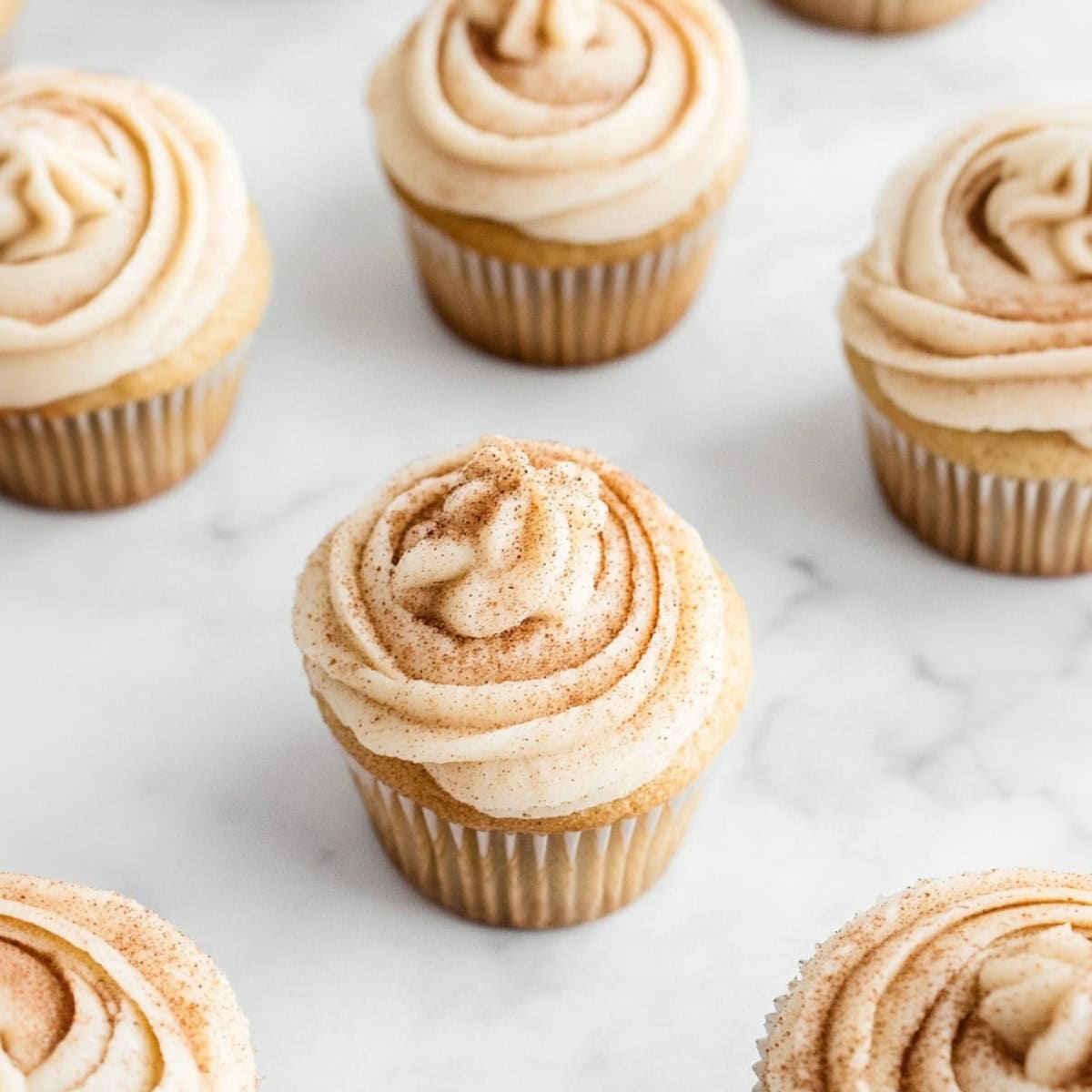 Snickerdoodle cupcakes with cream cheese frosting on a marble table.